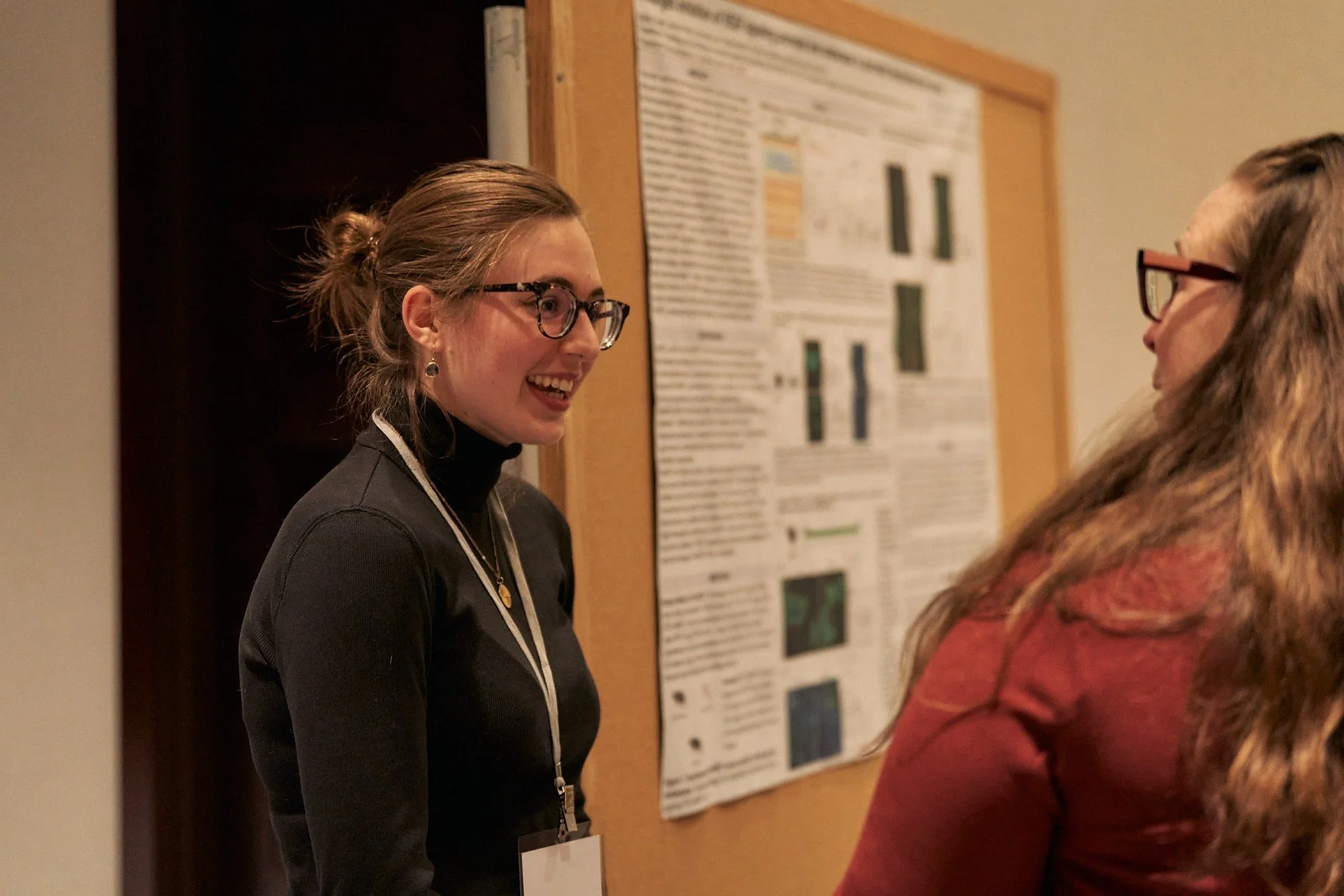 Two women having a conversation at a scientific conference, with a research poster on the wall behind them.