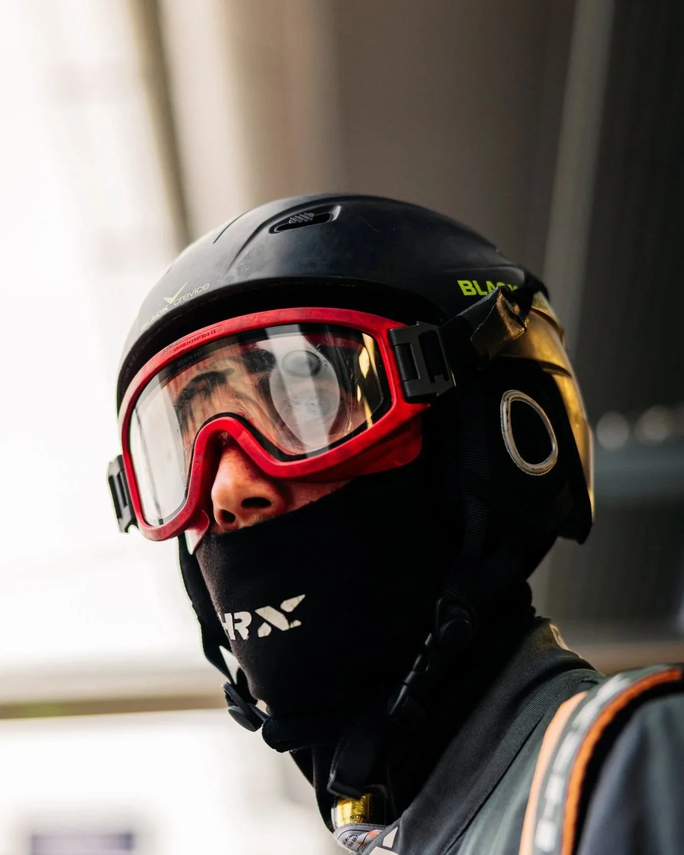 A person wearing a black helmet, red goggles, and a black face covering.