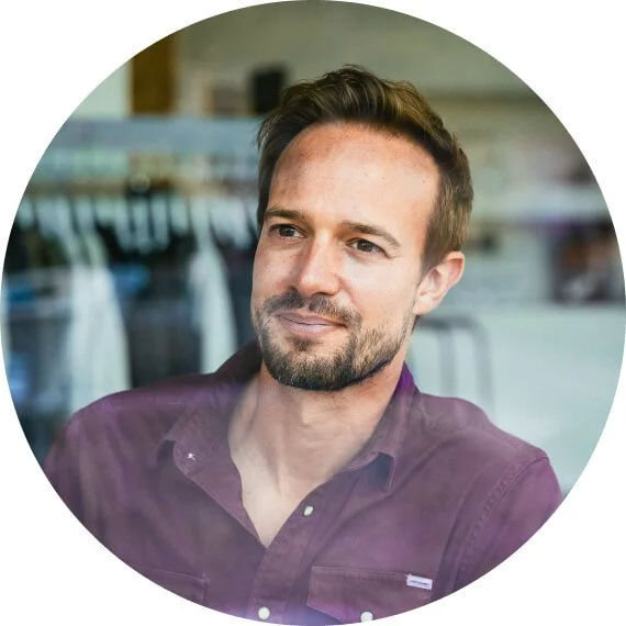 A man with short brown hair and a beard, wearing a dark purple shirt, sitting in a laundromat.