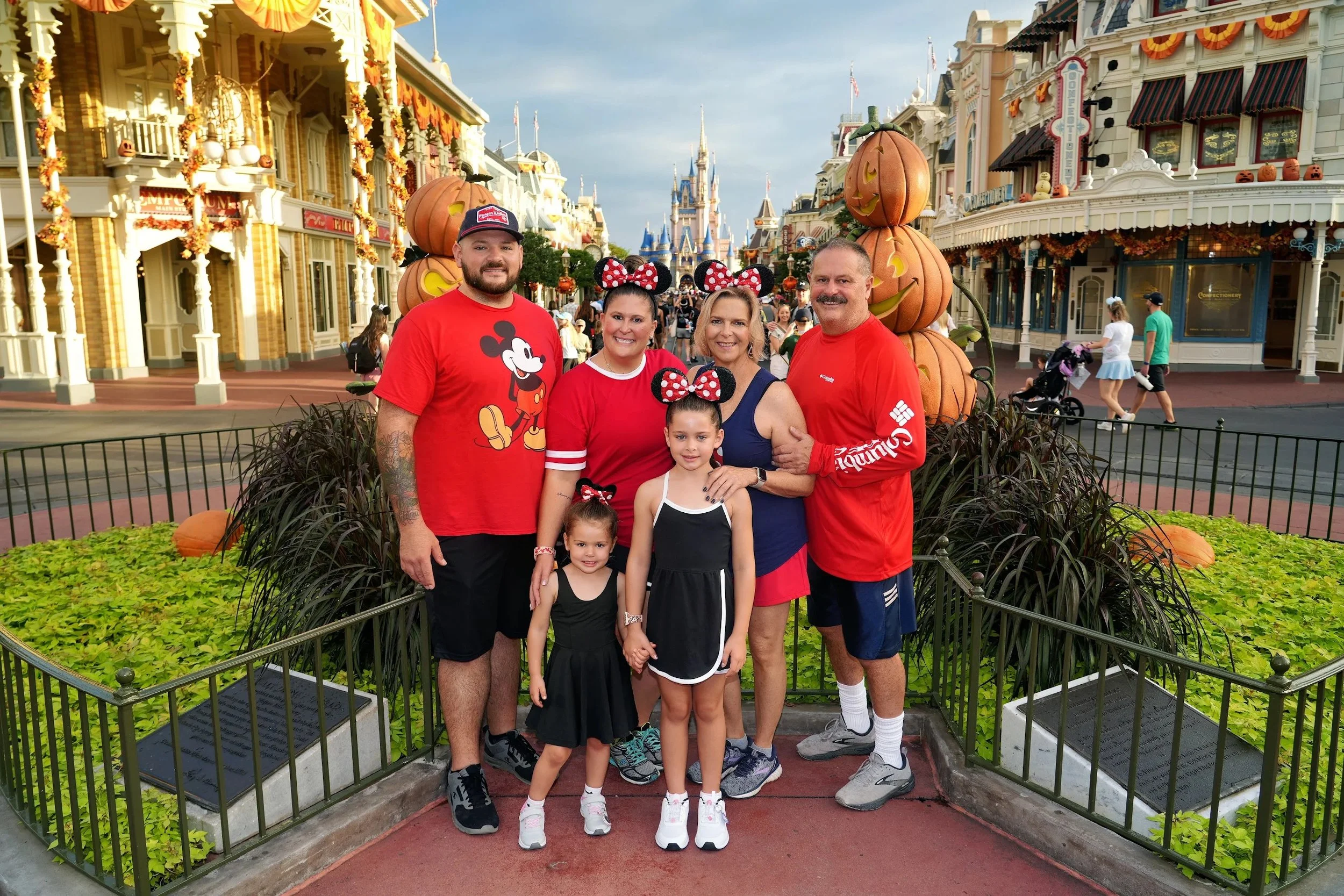 Family of six posing in front of a pumpkin display at Disney World with castle in the background, decorations for Halloween, and other visitors in the background.