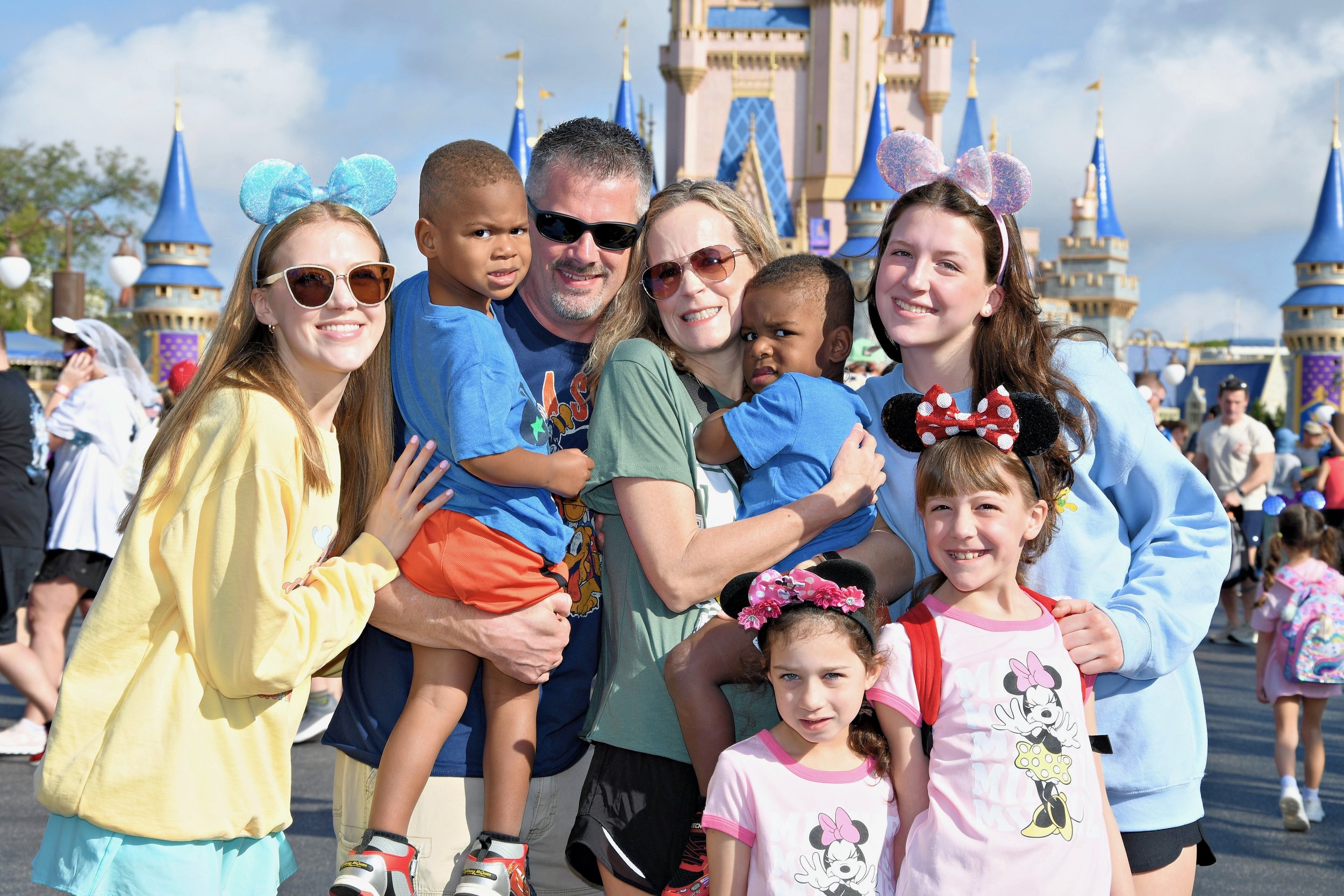 Family group at Disney World, including adults and children wearing Minnie Mouse ears, posing in front of Cinderella Castle.