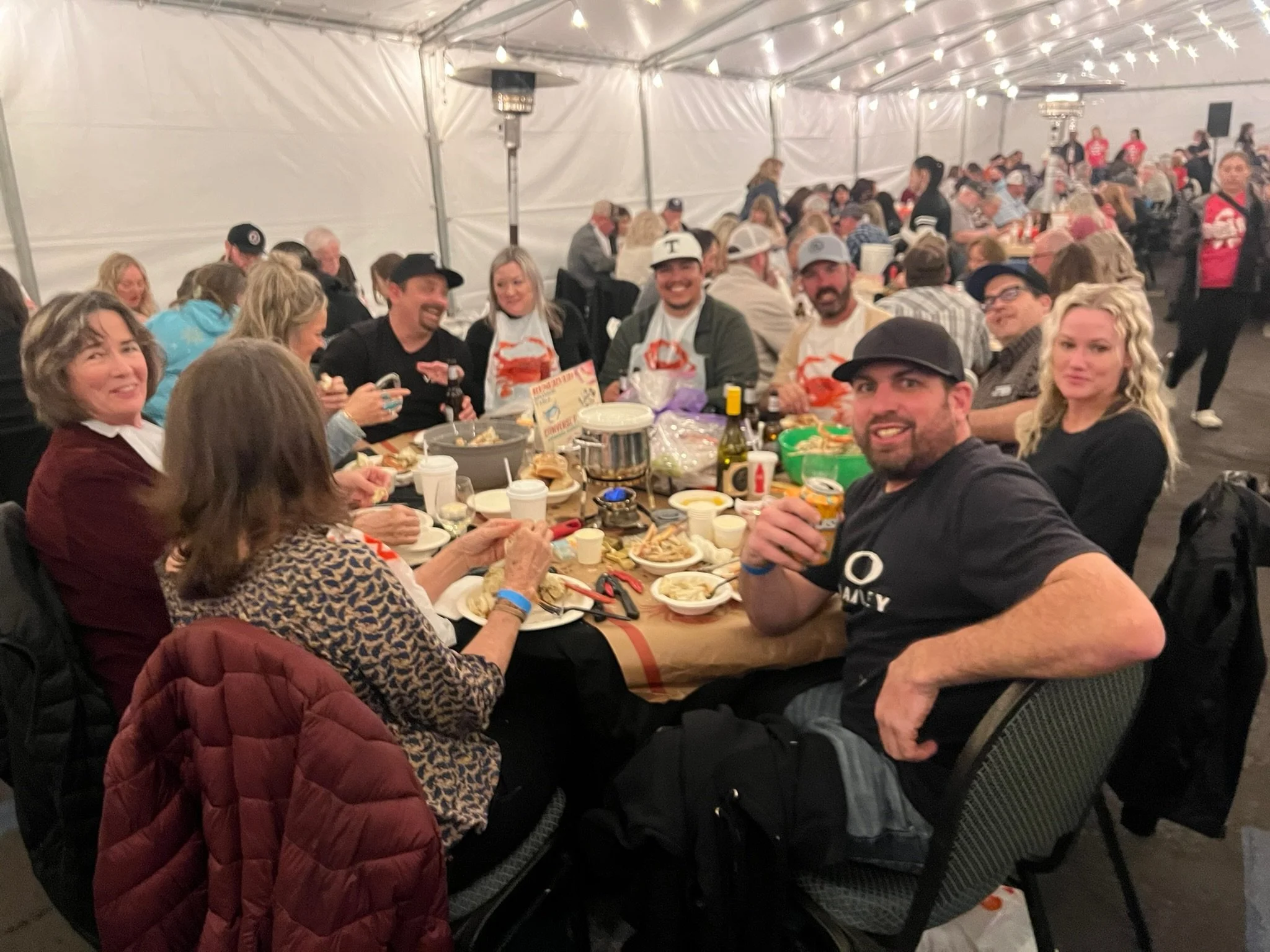 People sitting around a banquet table at a celebration in a large tent, smiling and enjoying food.