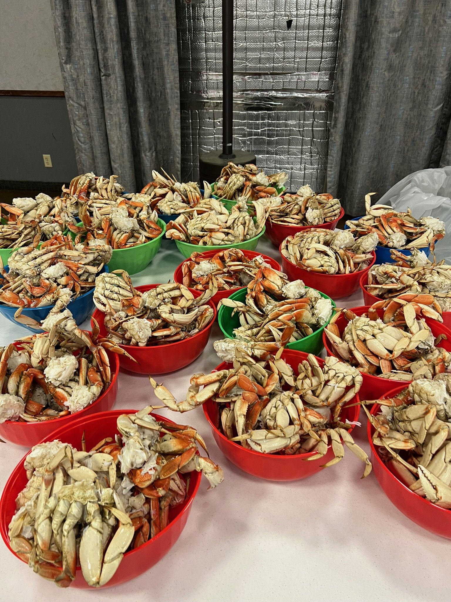 Multiple bowls filled with cooked crab legs on a table, with a curtain and a metallic insulation wall in the background.