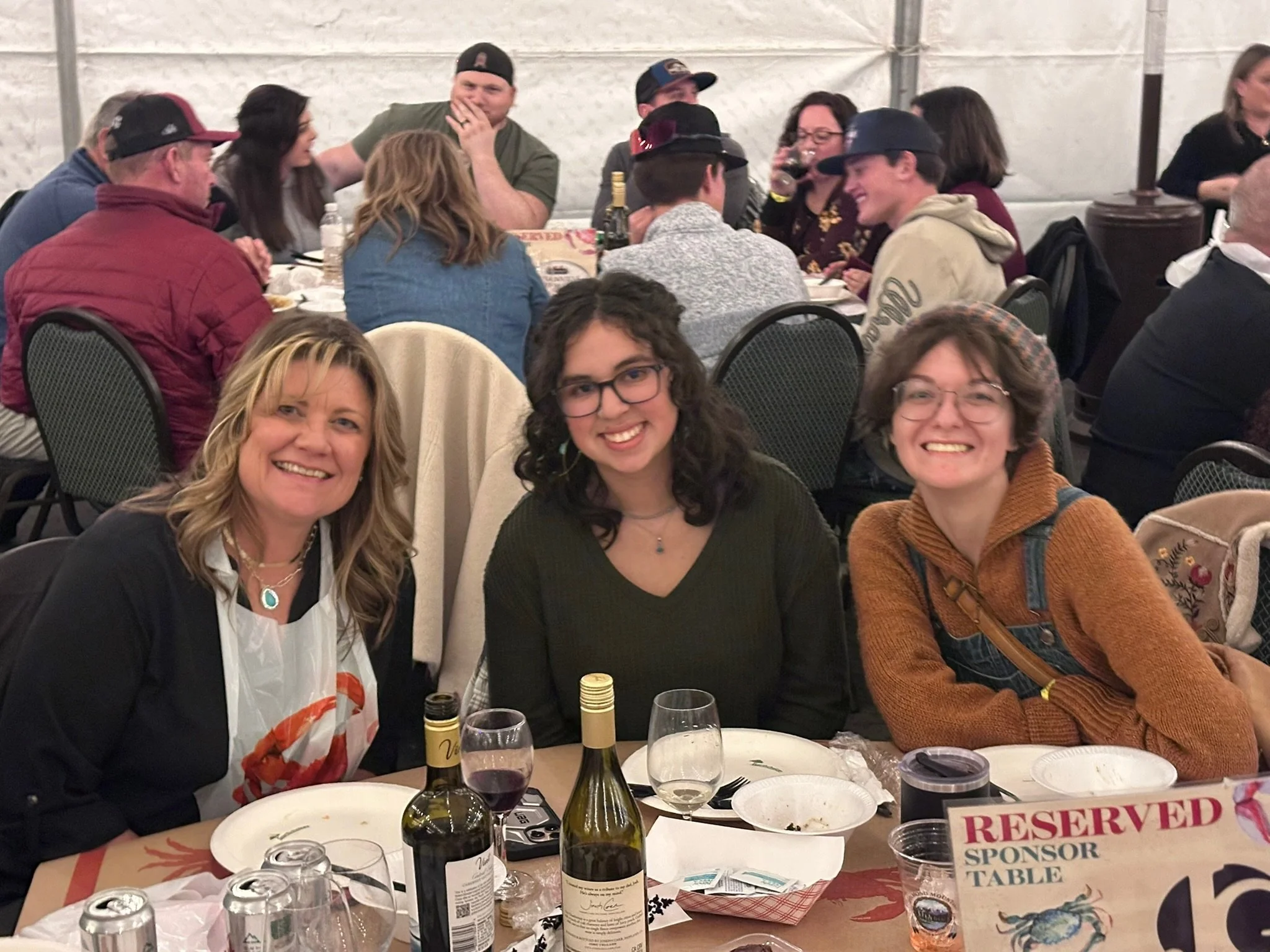 A group of people sitting around a table at a social gathering, smiling and talking, with food, beverages, and a "RESERVED" sign on the table.