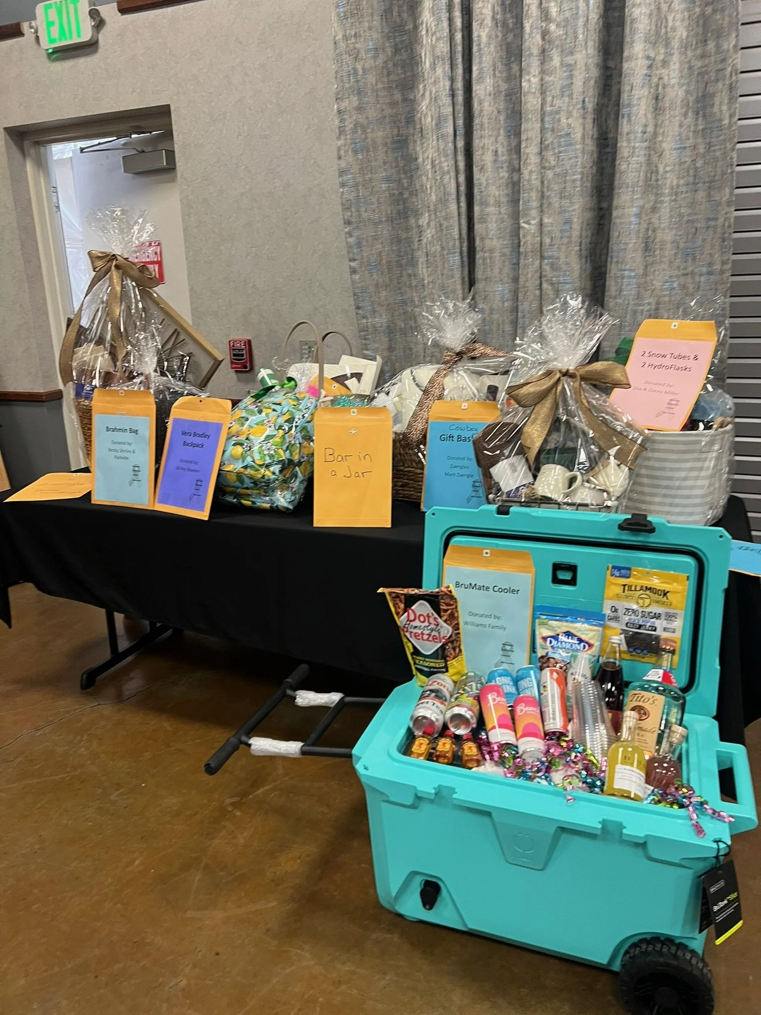 Table with various gift baskets and items, some wrapped in clear plastic with ribbon, and a blue container filled with party favors and candies.