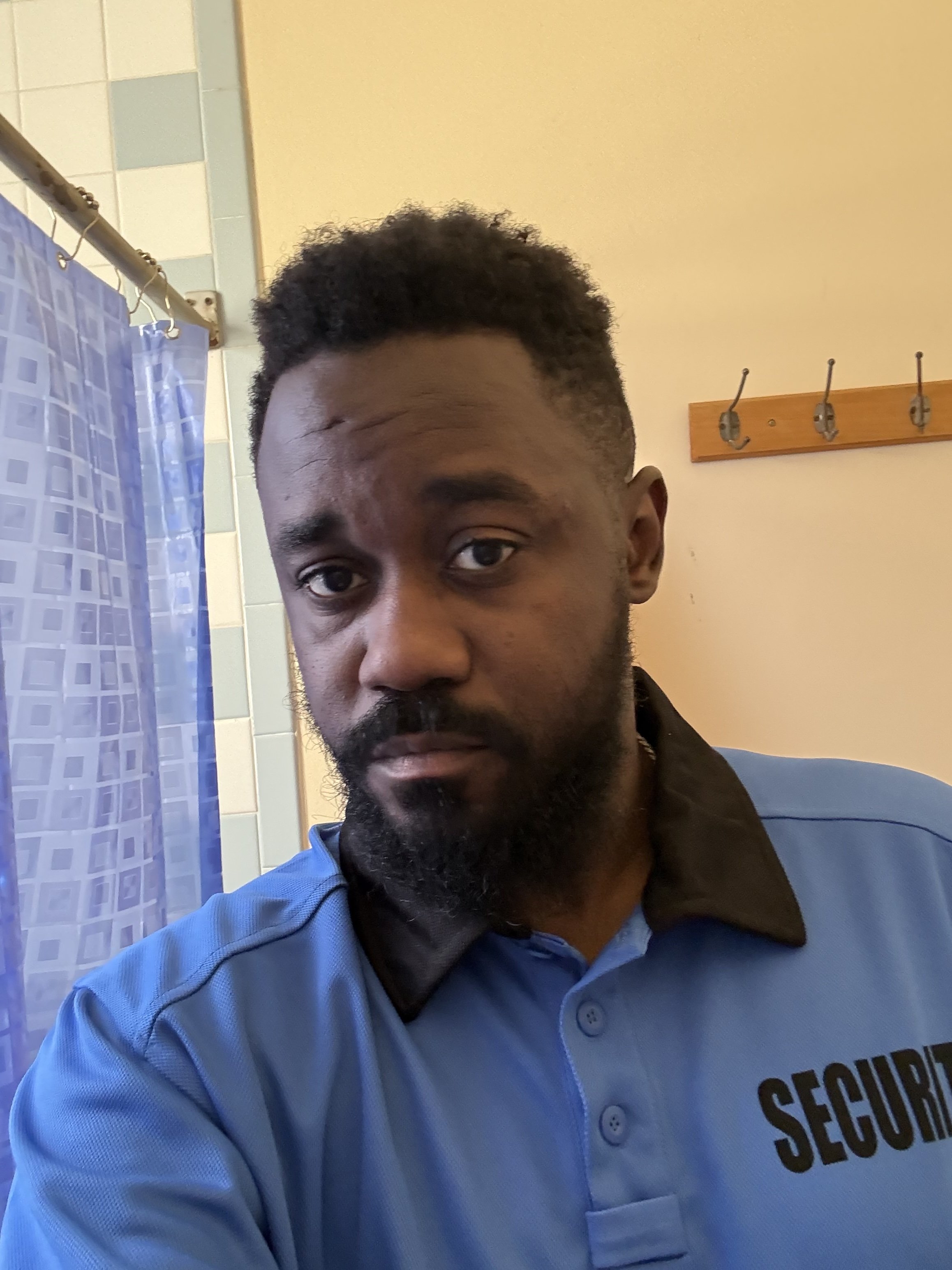 Fedly Daniel in costume as a security guard on the set of an experimental short film, wearing a blue security uniform and looking directly into the camera.