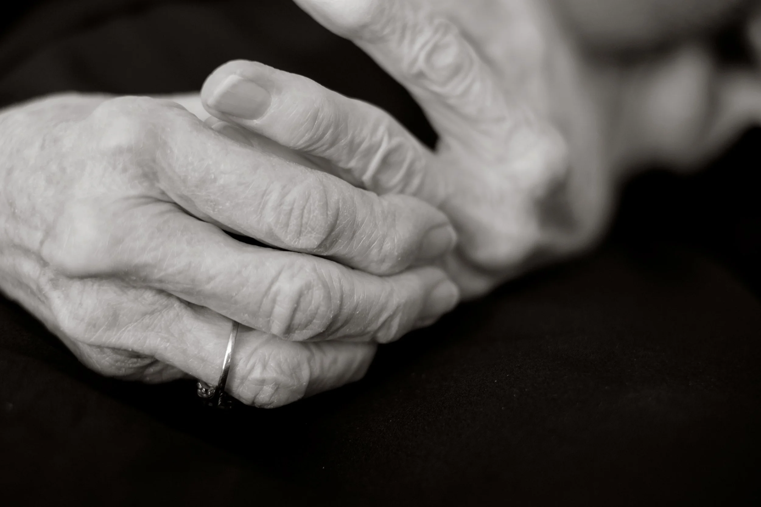Close-up of elderly hands with visible veins and wrinkles, resting on each other, black and white photograph.