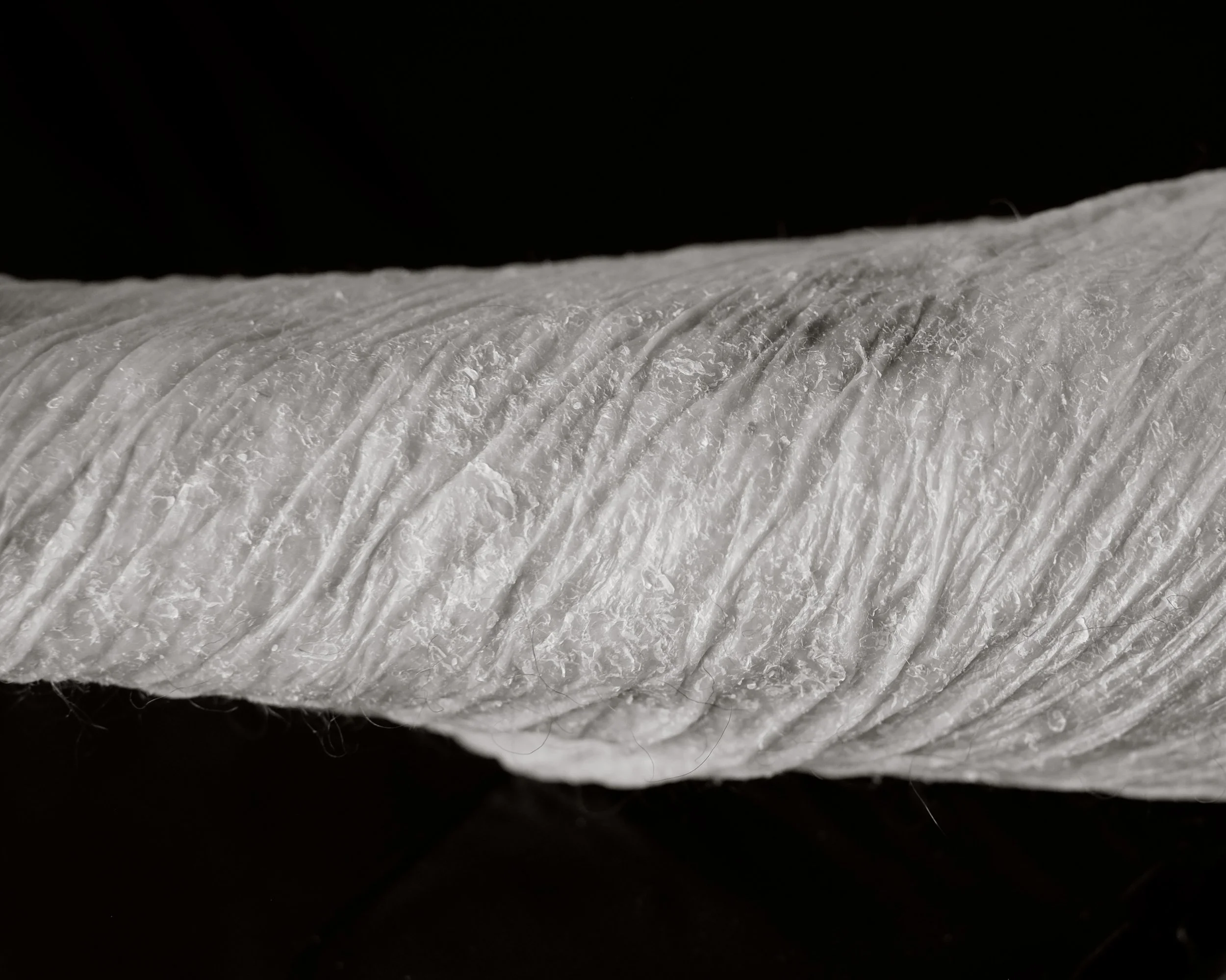 Close-up of a white, textured, spun fiber thread or yarn against a black background.