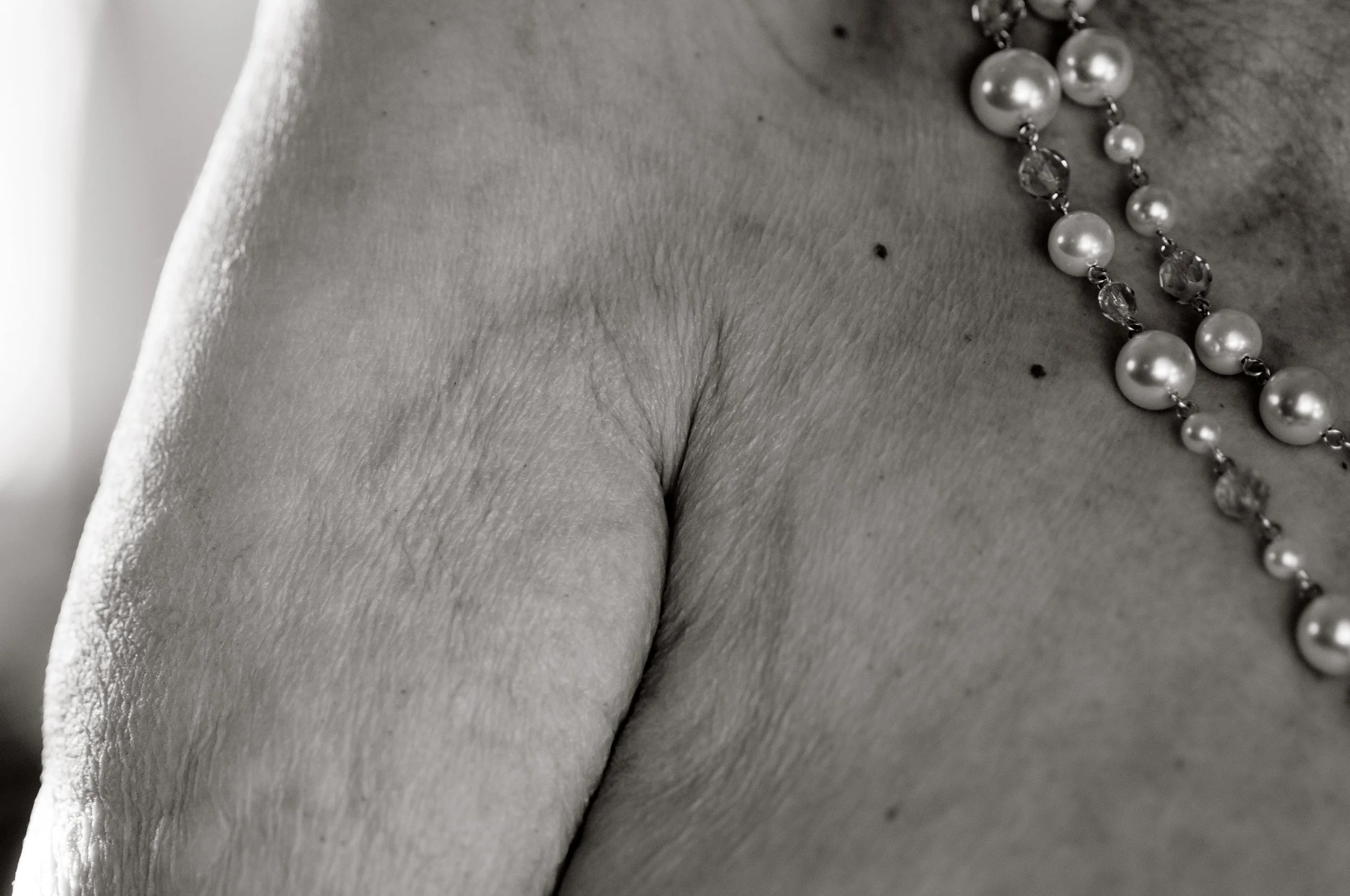 Close-up black-and-white photo of an older woman's chest with a pearl necklace.