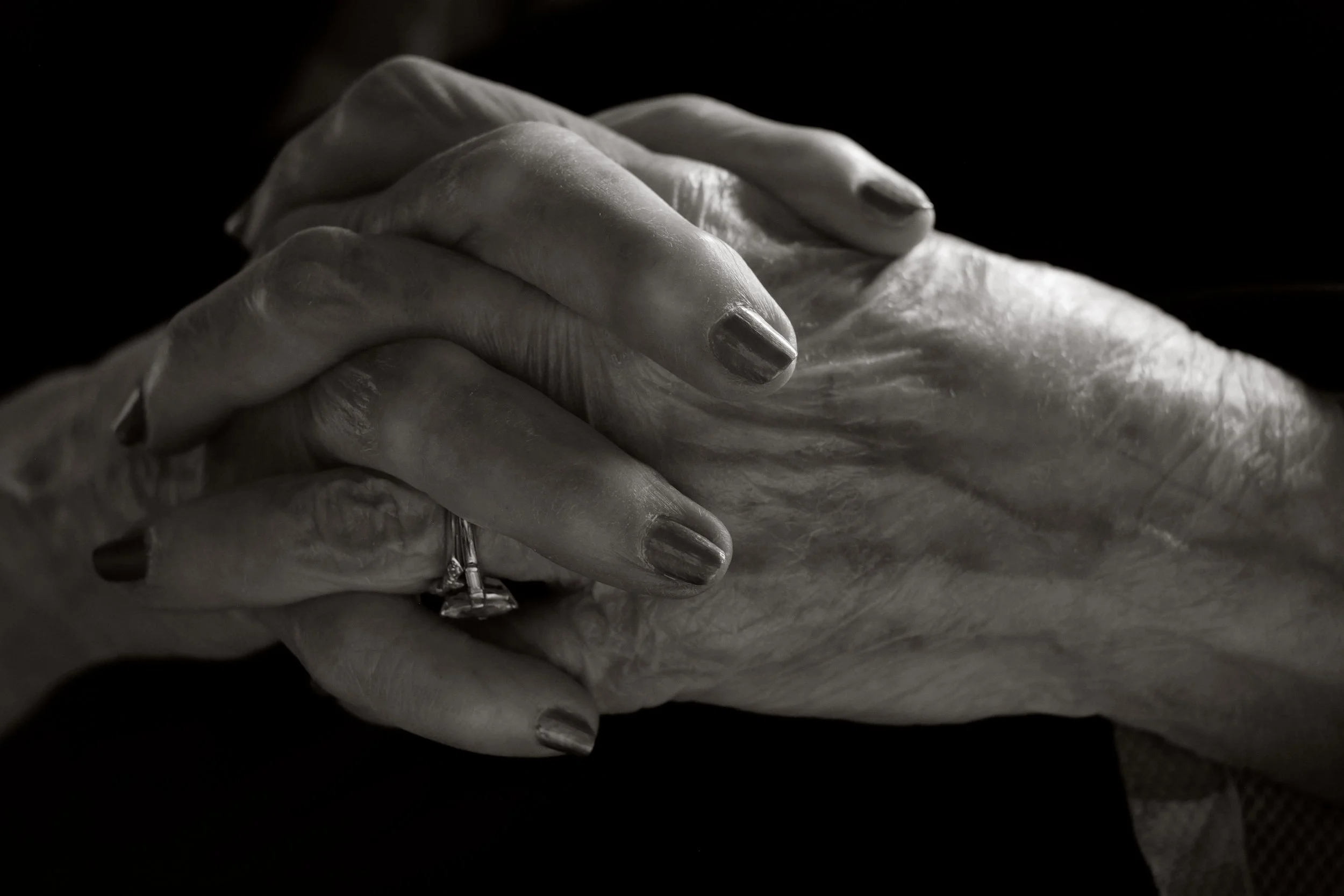 Close-up of two hands gently clasped together, one with a ring, in black and white.
