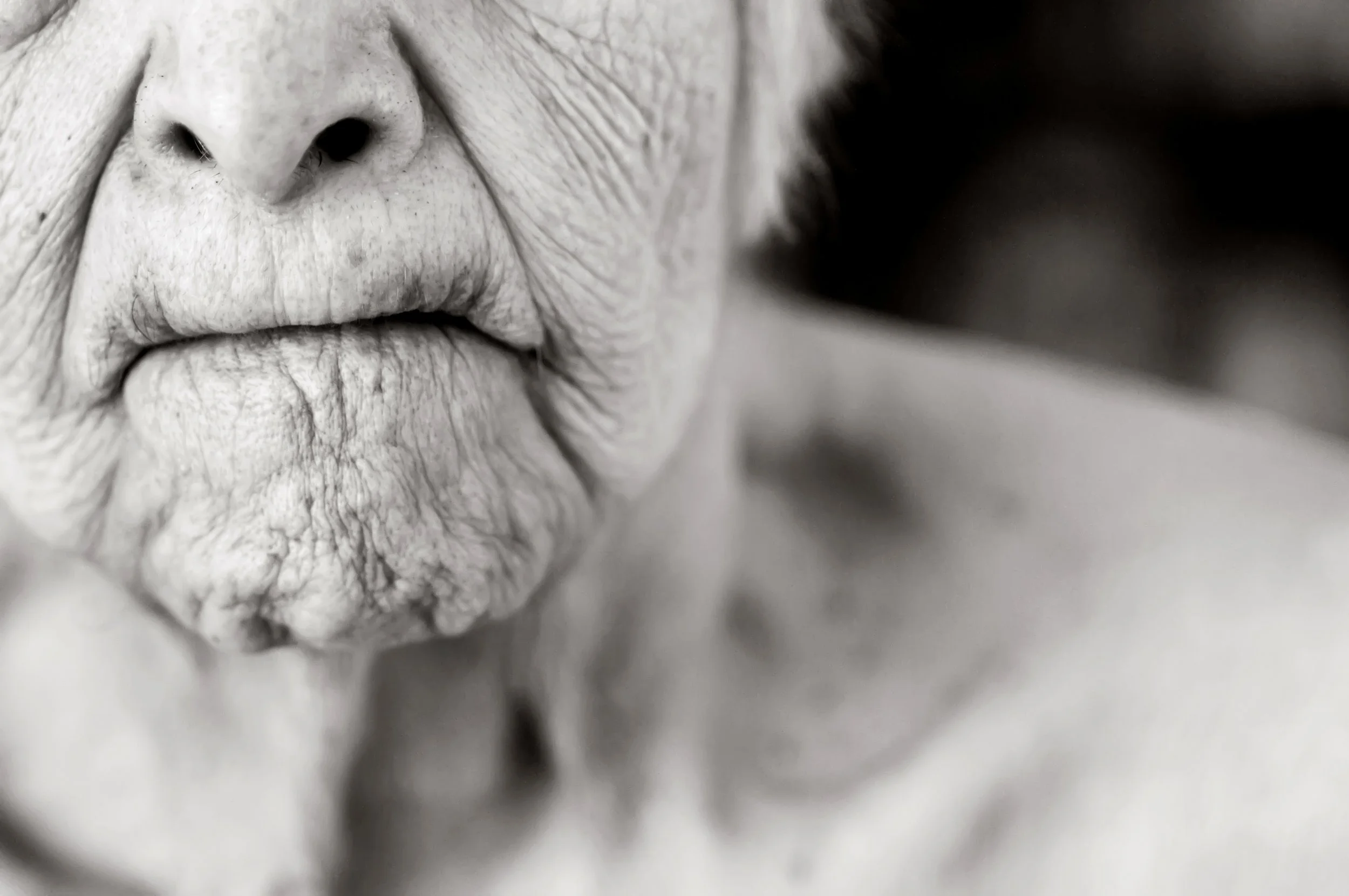 Close-up of the lips and nose of an elderly person with wrinkled skin in black and white.
