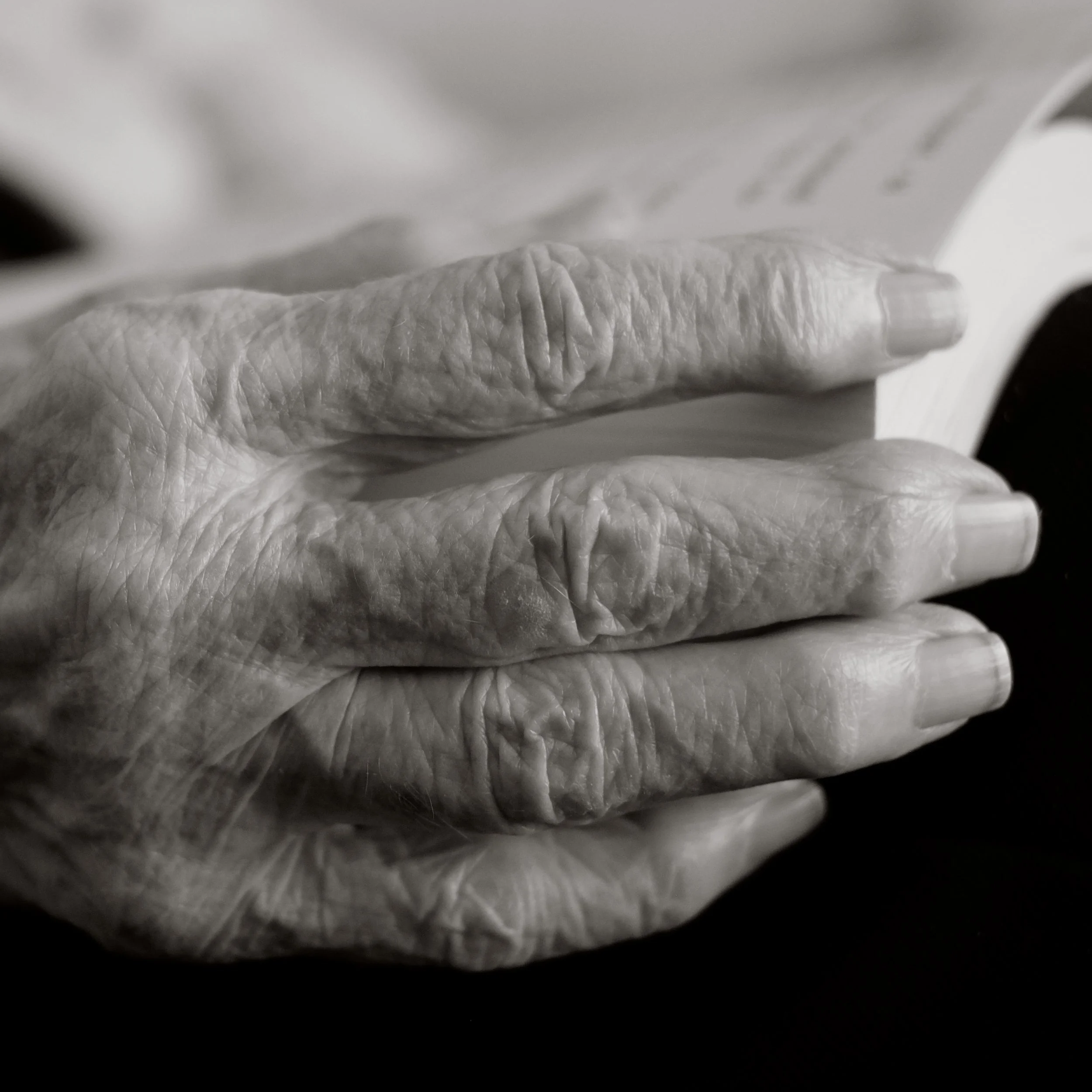 Close-up of elderly person's hand resting on a surface, showing wrinkled skin and nails.