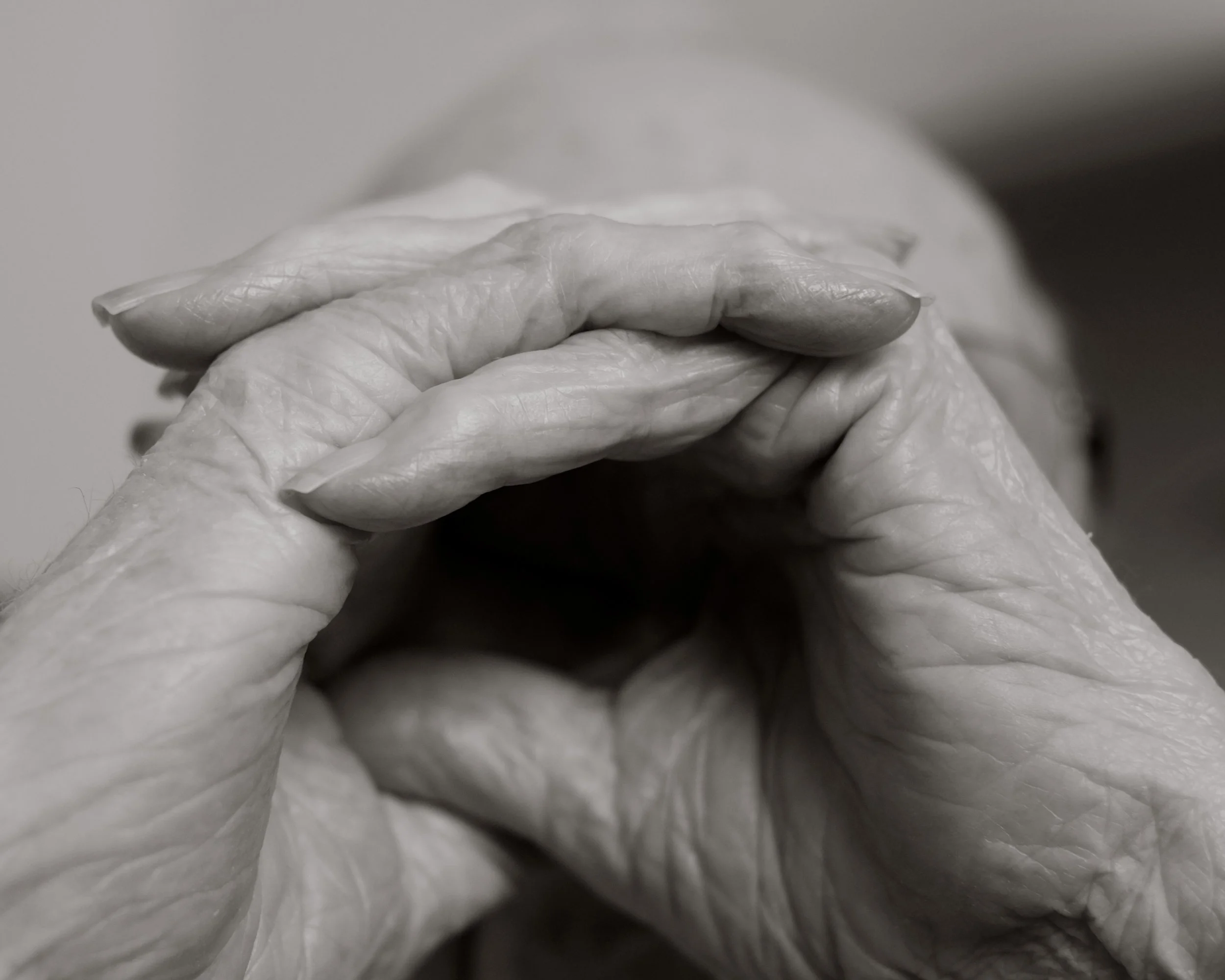 Close-up of elderly hands clasped together in prayer, black-and-white photograph.