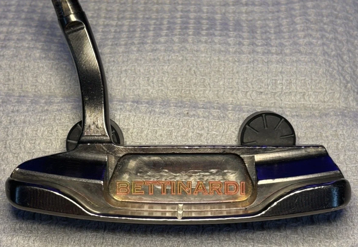 Close-up of a Bettinardi golf putter lying on a textured surface.