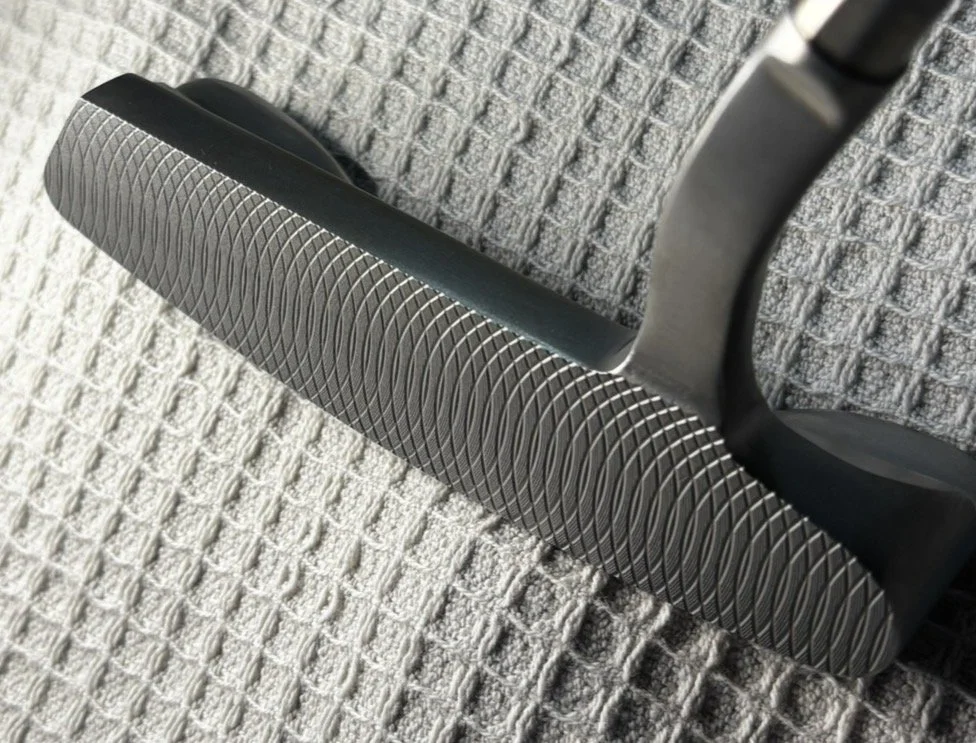 Close-up of a golf putter club resting on a textured gray fabric surface.
