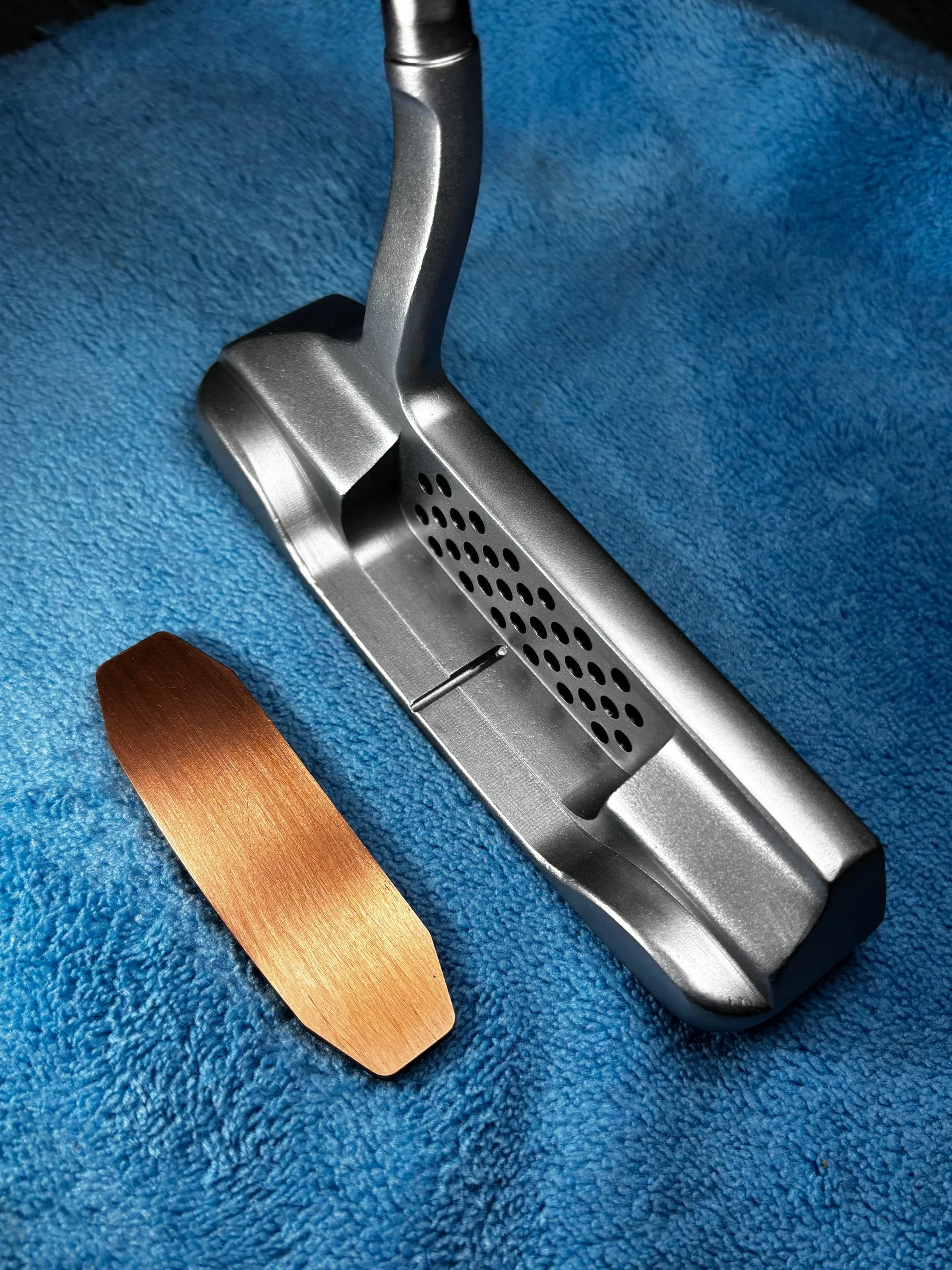 A golf club and a copper-colored golf tee on a textured blue surface.