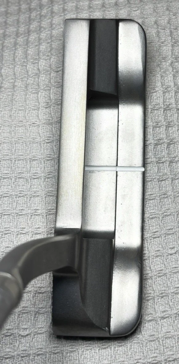 Close-up of a golf putter head on a textured surface.