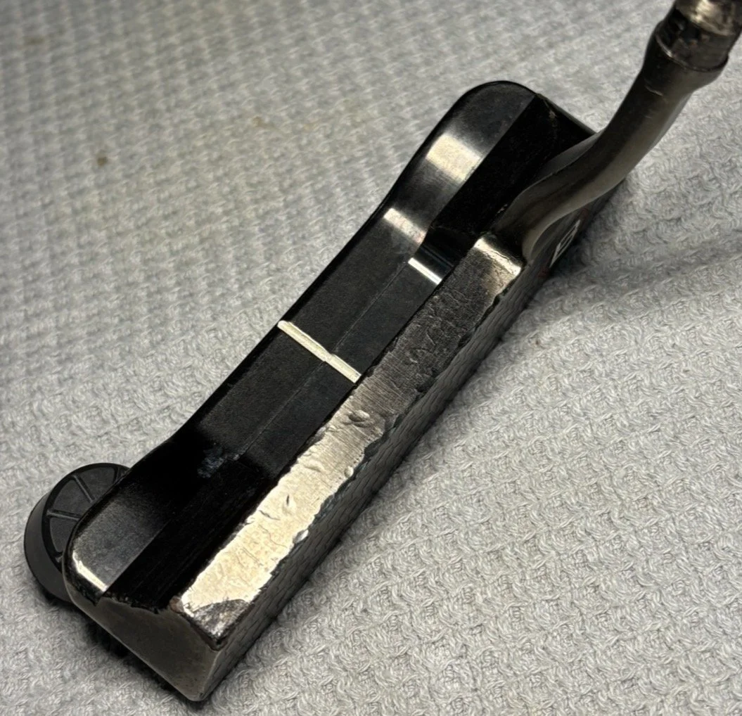 Close-up of a black curling iron with a burnt, damaged cord resting on a light gray textured surface.