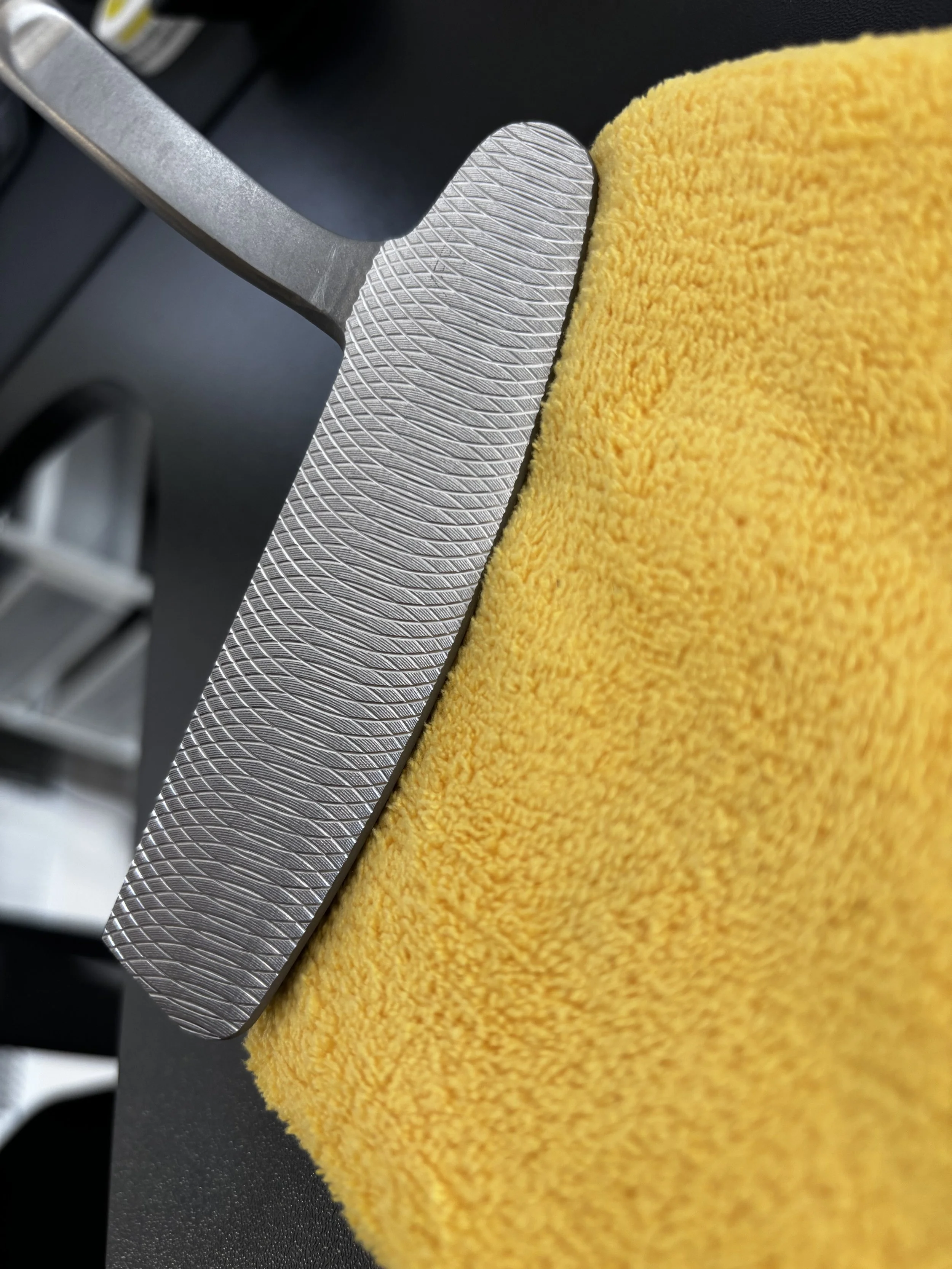 Close-up of a metal object with intricate textured patterns next to a bright yellow microfiber cloth on a black surface.