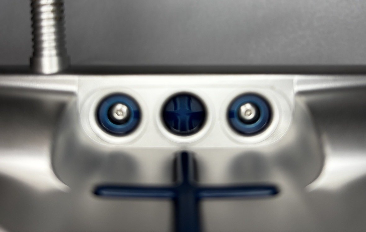 Close-up of a mechanical component with two blue circular parts and a central black circle with blue cross marking, mounted on a metal surface.