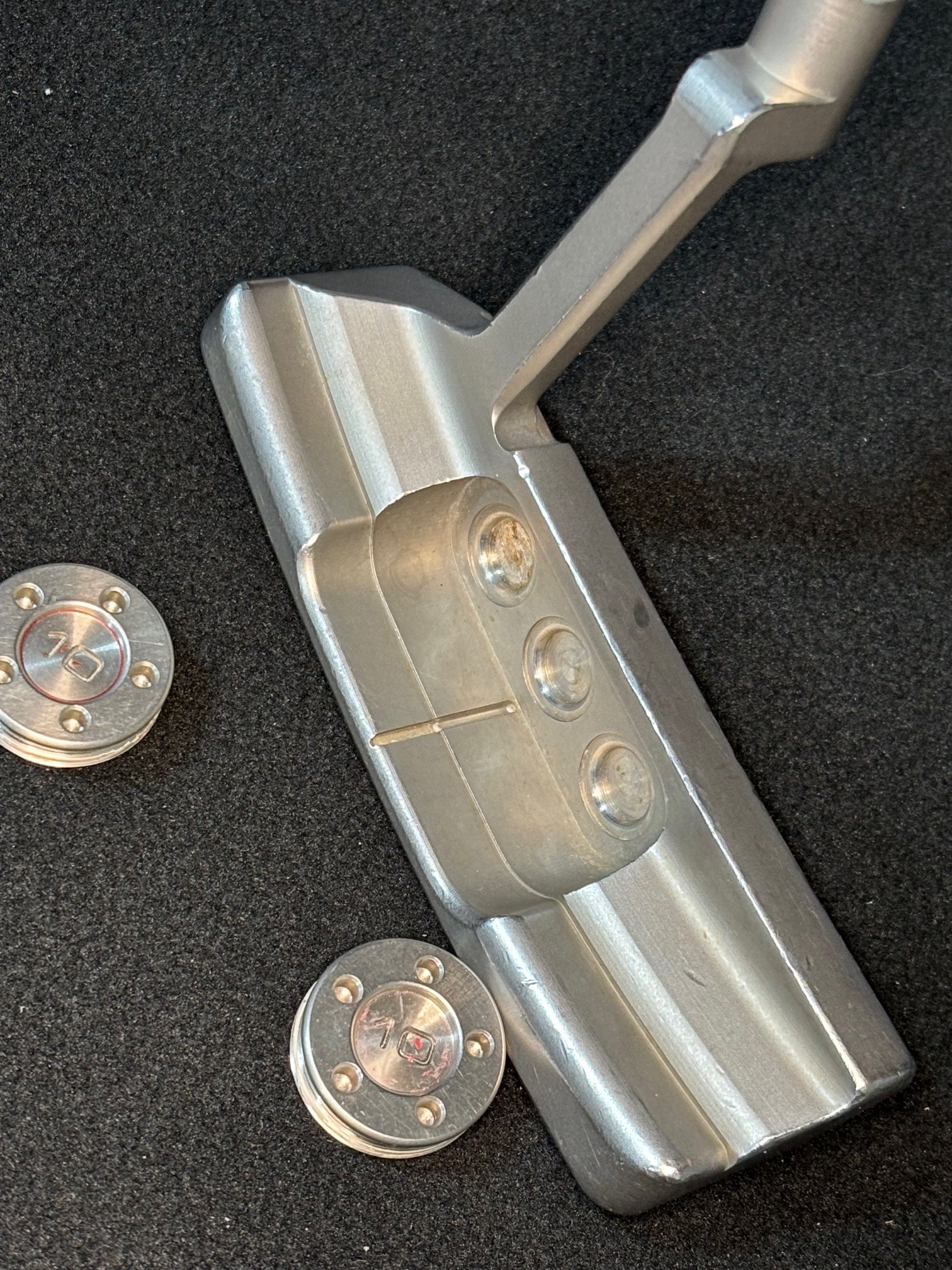 Close-up of a metallic car hinge on a black surface with a few metallic bolts nearby.