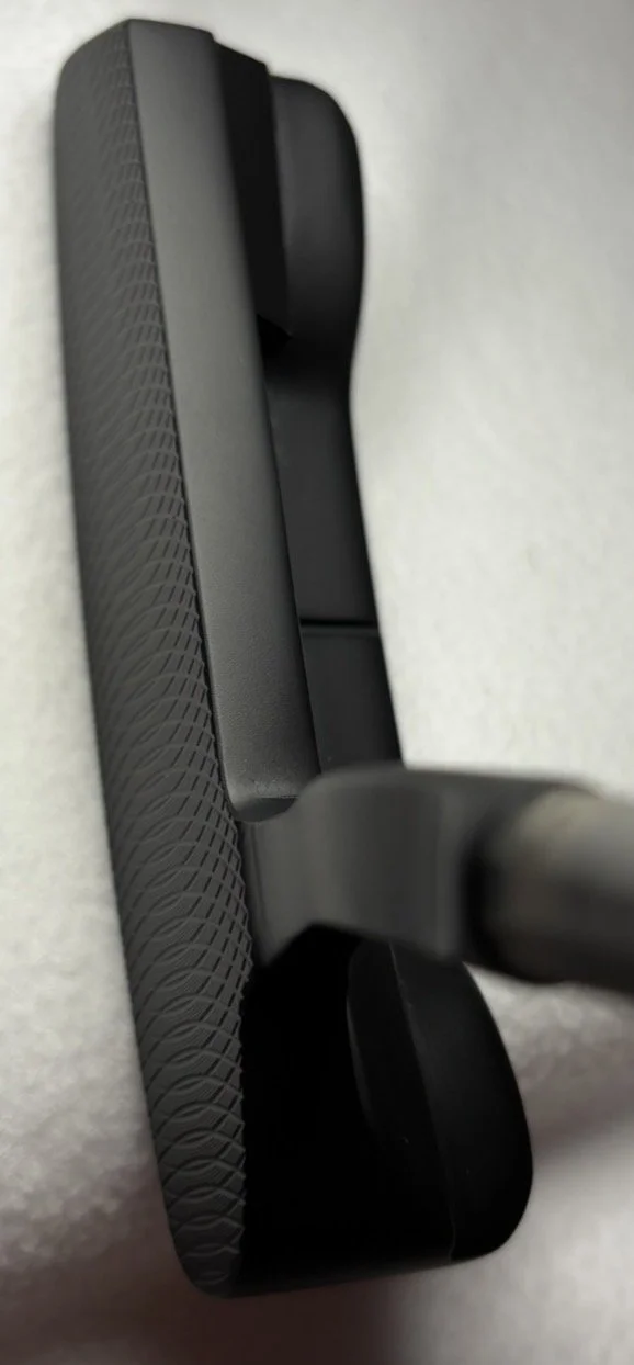 A black hairbrush with a textured grip on one side, placed on a light-colored surface.
