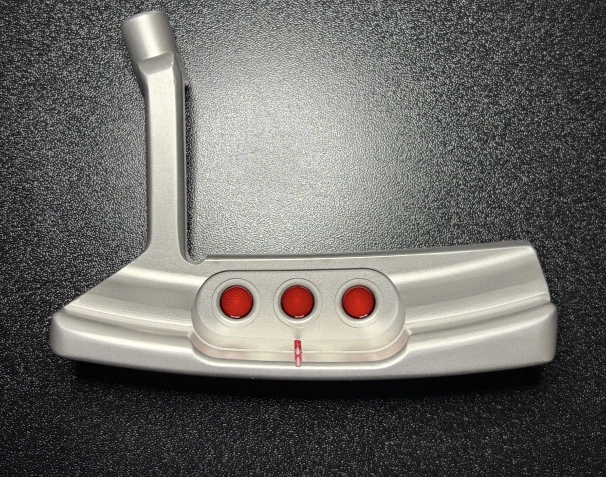 A golf putter with three red indicator lights on the base, resting on a textured black surface.