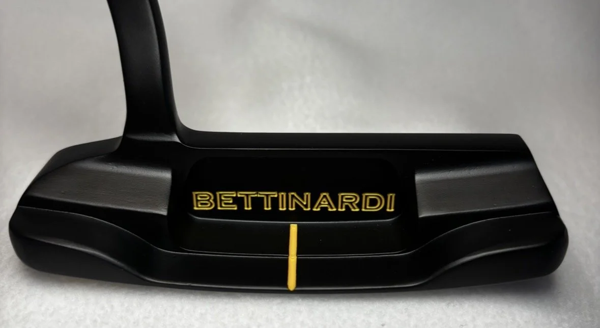 A Bettinardi golf putter with a black finish and a yellow alignment line.