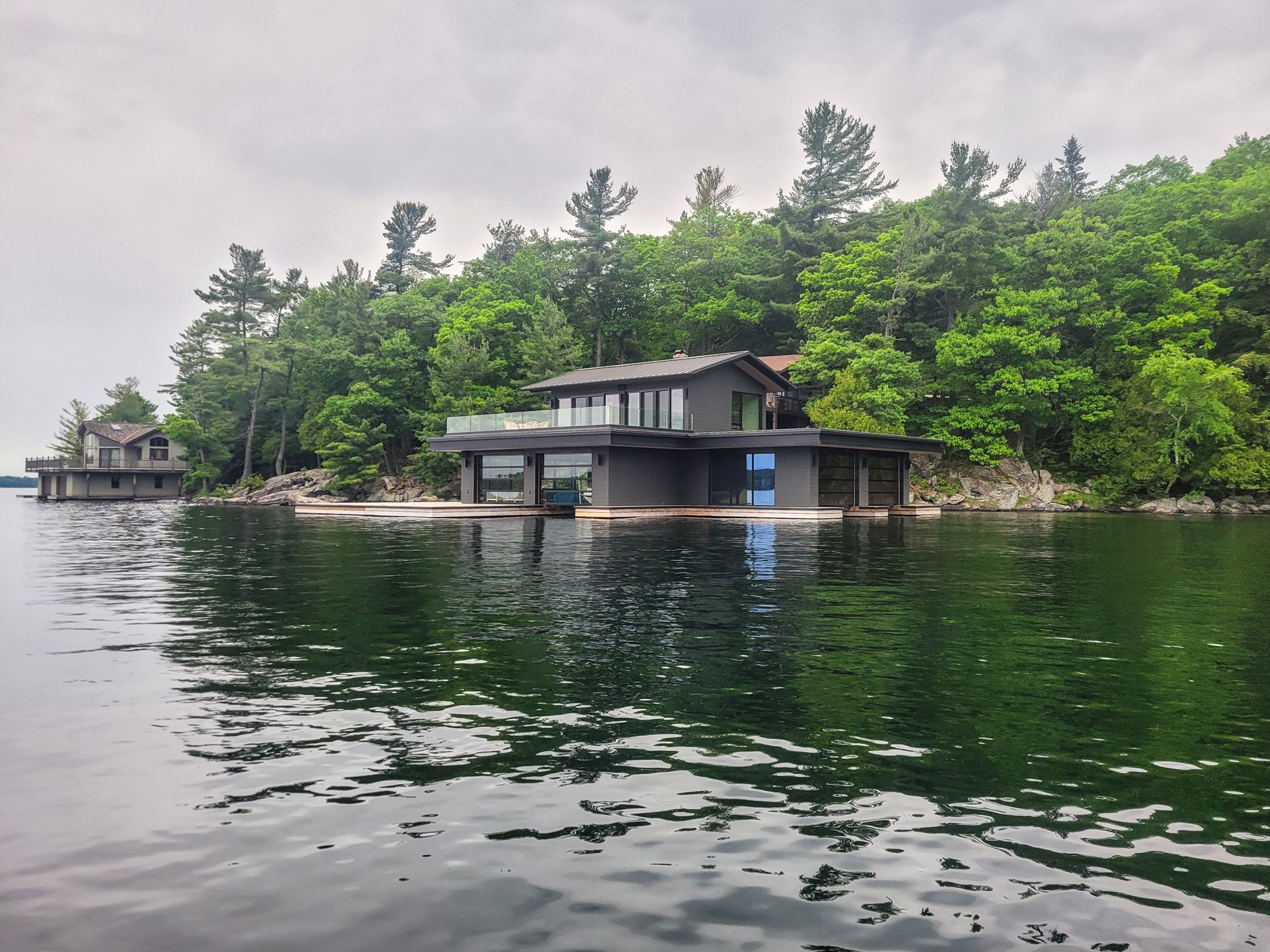 Modern house on a lake with surrounded by lush green trees, overlooking calm water.