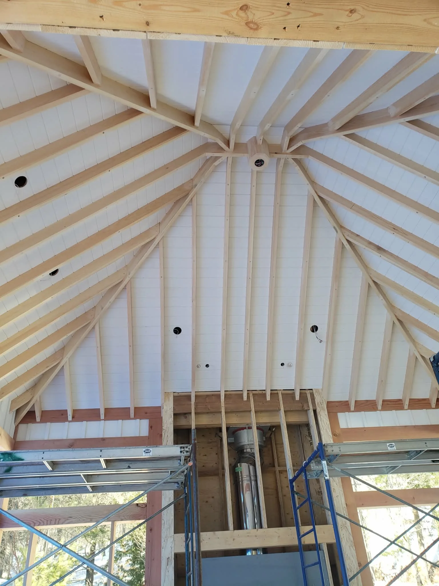 Interior of a building under construction with a vaulted wooden ceiling, exposed beams, and scaffolding, showing framing and unfinished roof.