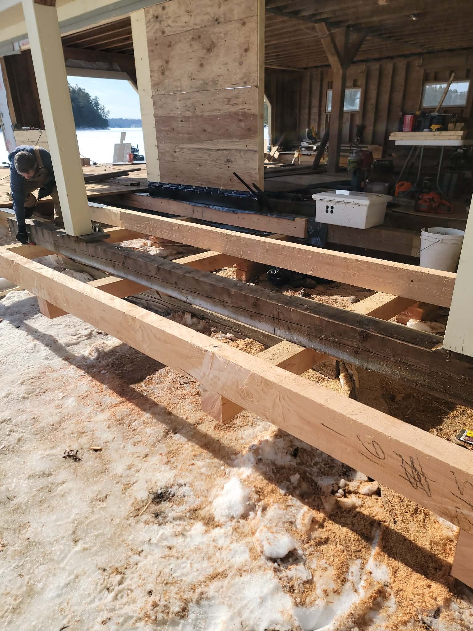 Construction site with wooden beams and workers building a house near a lake.