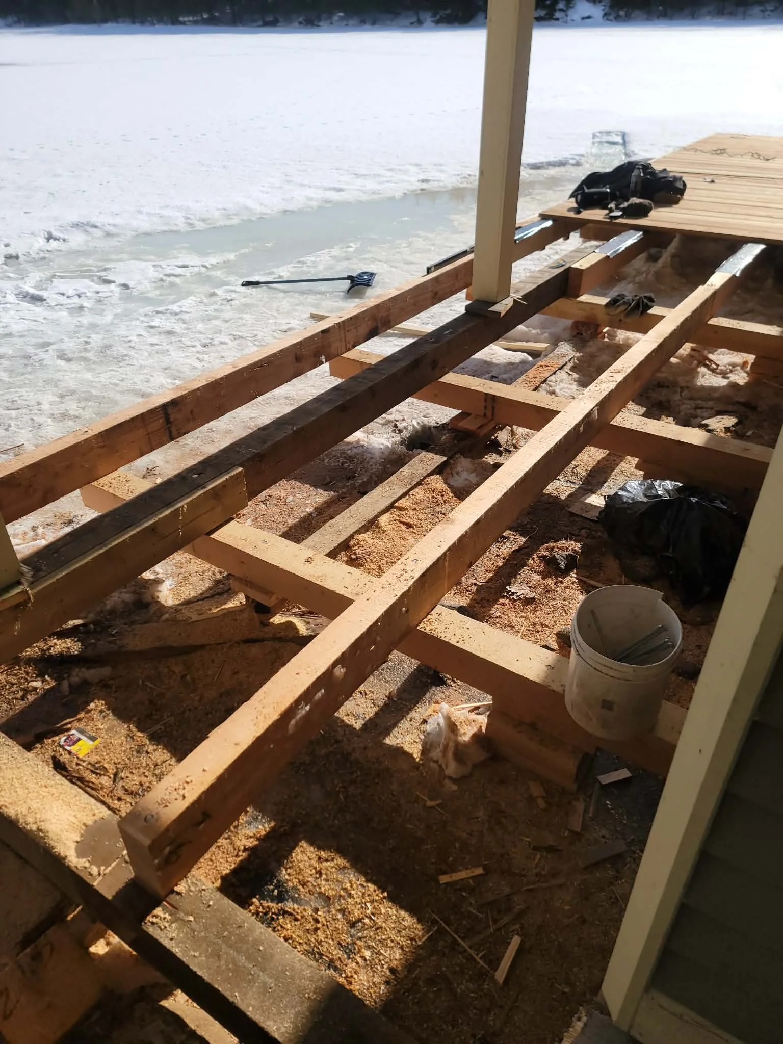Construction of a deck by a frozen body of water, showing wooden framing, construction tools, and materials.