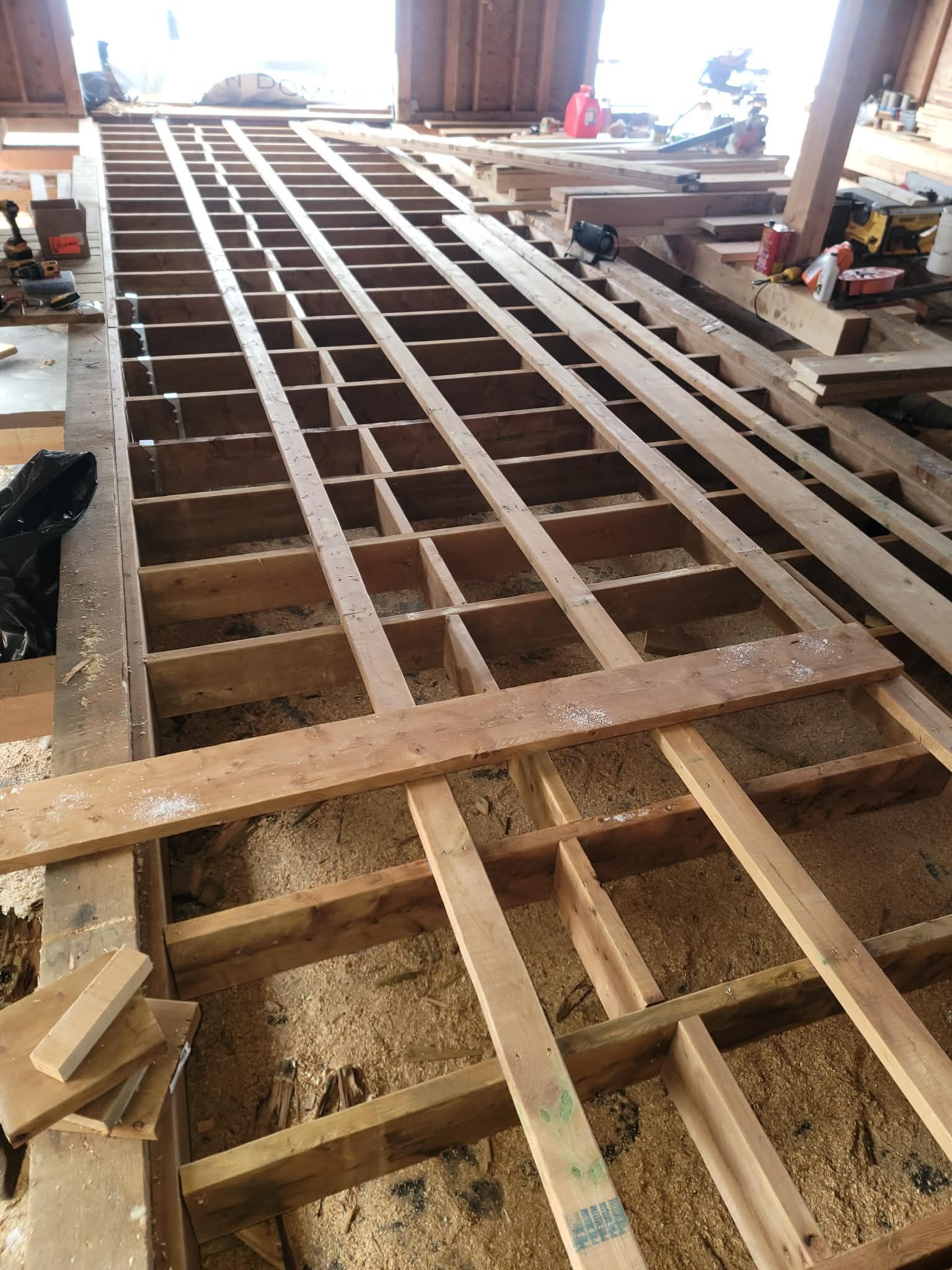 Wooden floor framing construction in progress with exposed joists and beams in a garage or workshop.