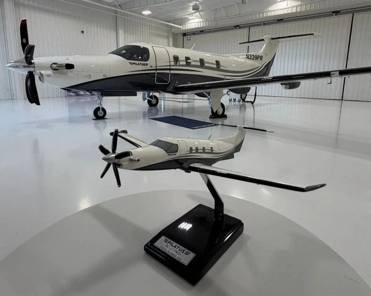 Avión y modelo a escala en un hangar con paredes blancas y piso brillante.