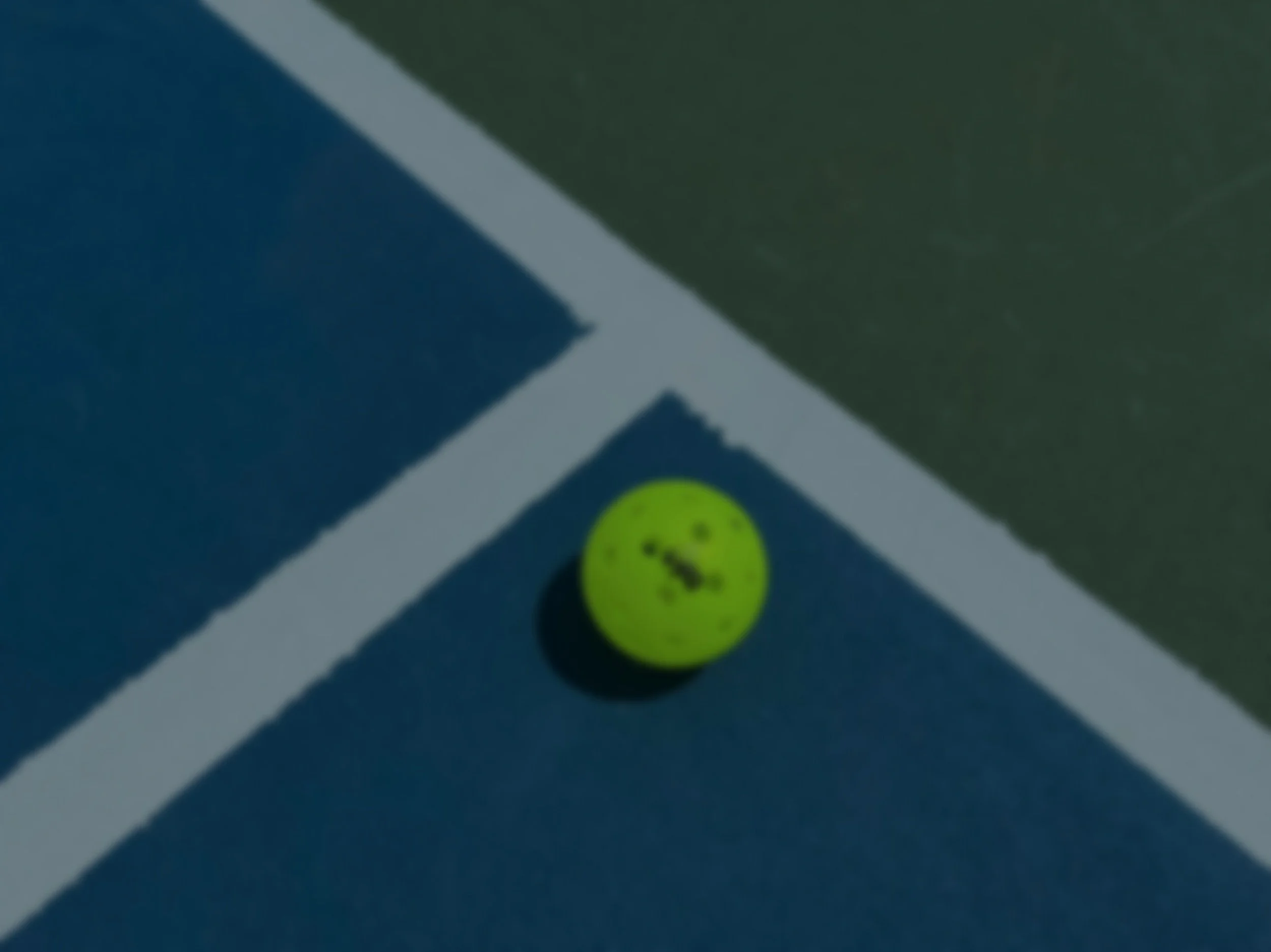 Close-up of a green tennis ball on a dark-colored tennis court.