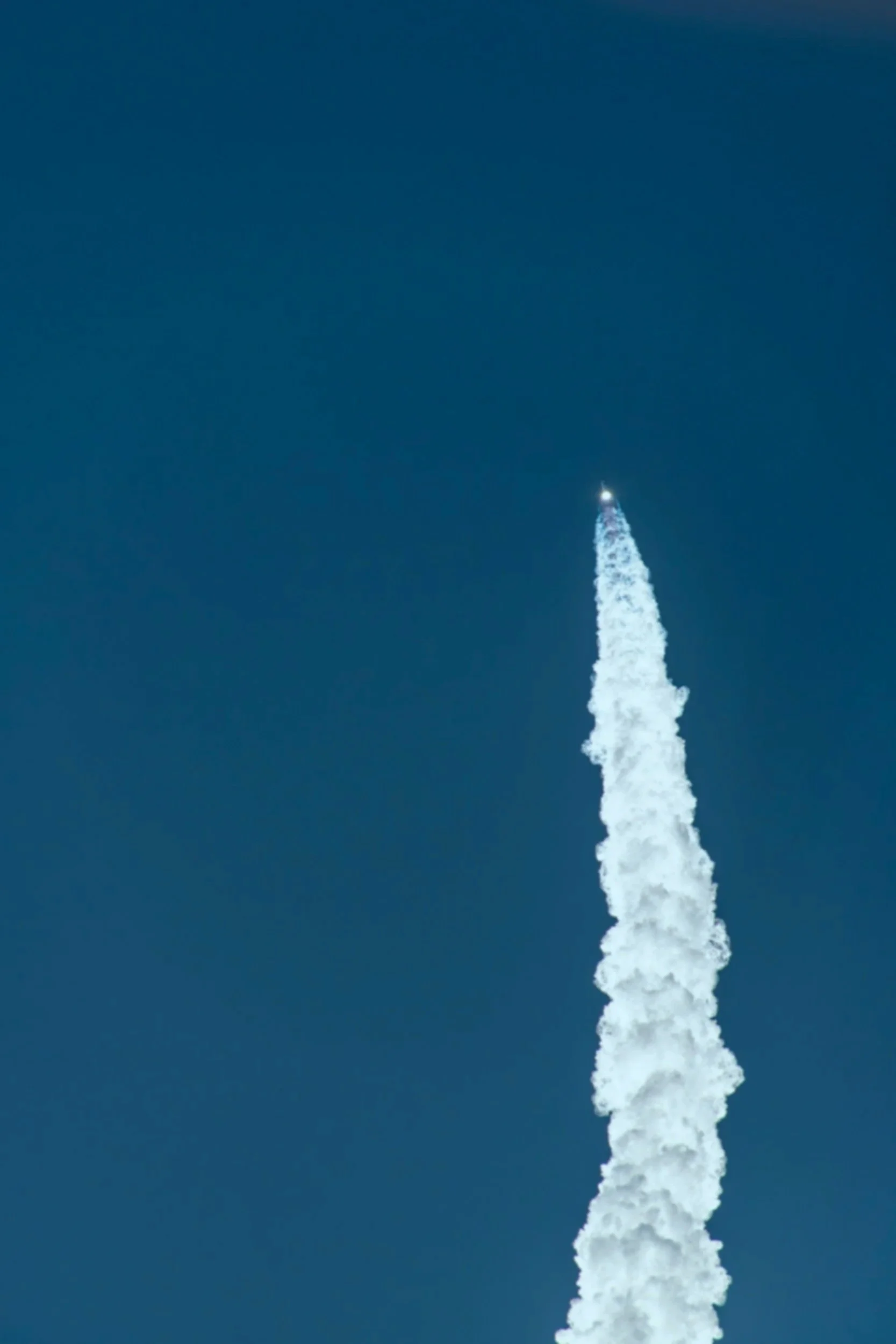 A rocket launching into the sky, leaving a trail of white smoke against a clear, dark blue sky.