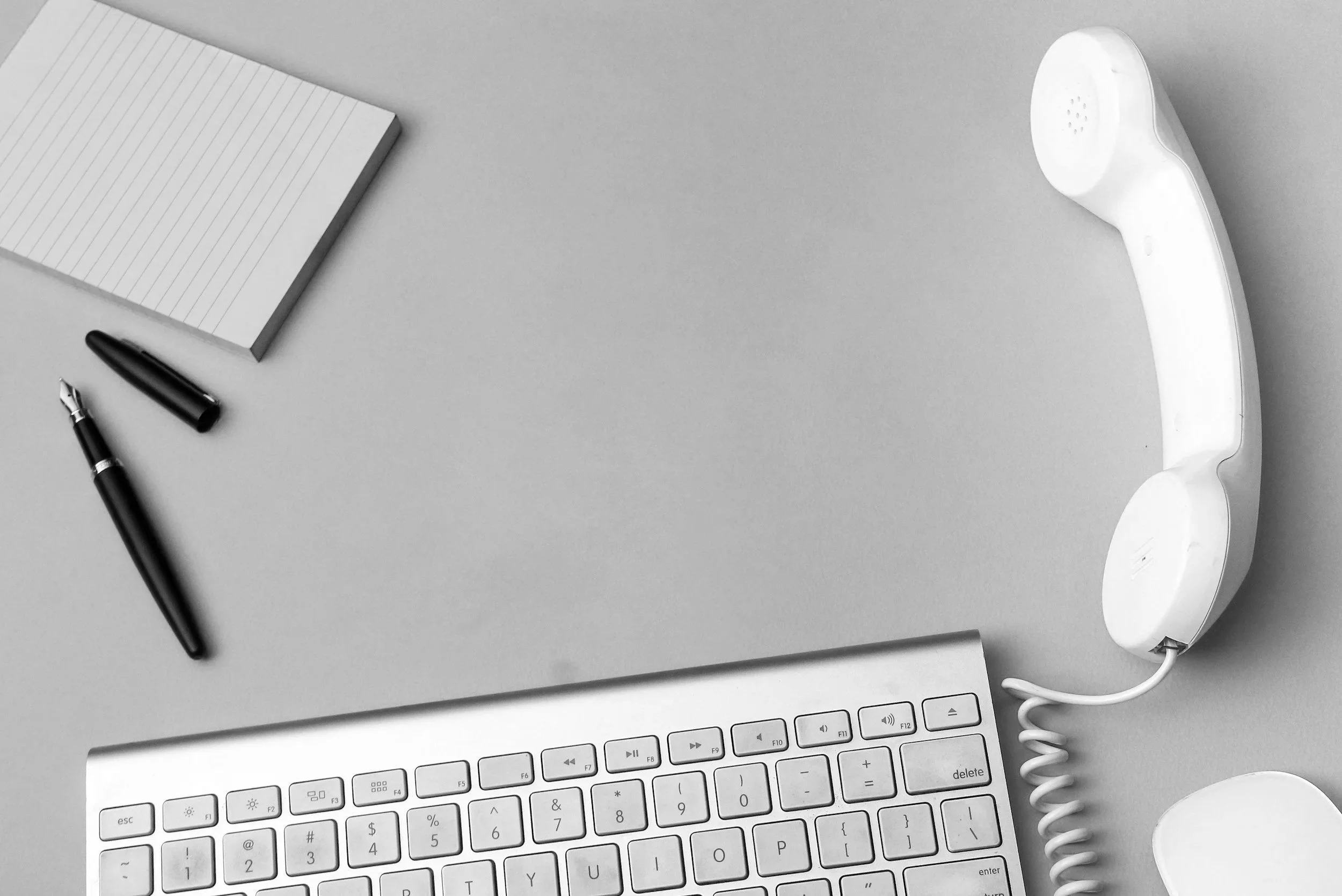 A computer keyboard, a notepad, a pen, a fingerprint scanner, and a telephone receiver arranged on a light gray surface.