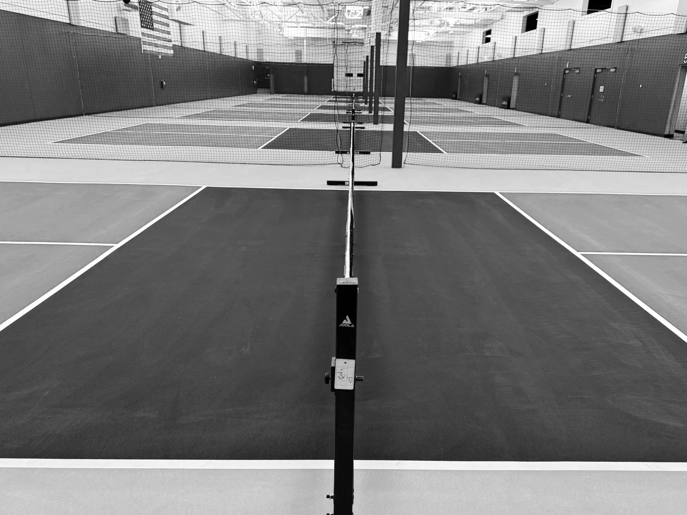Empty indoor pickleball court with a net in the center, multiple courts, and high ceiling.