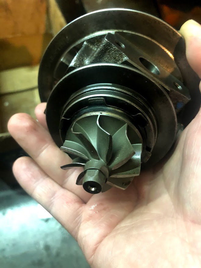 A person's hand holding a turbocharger cartridge with visible turbine blades.