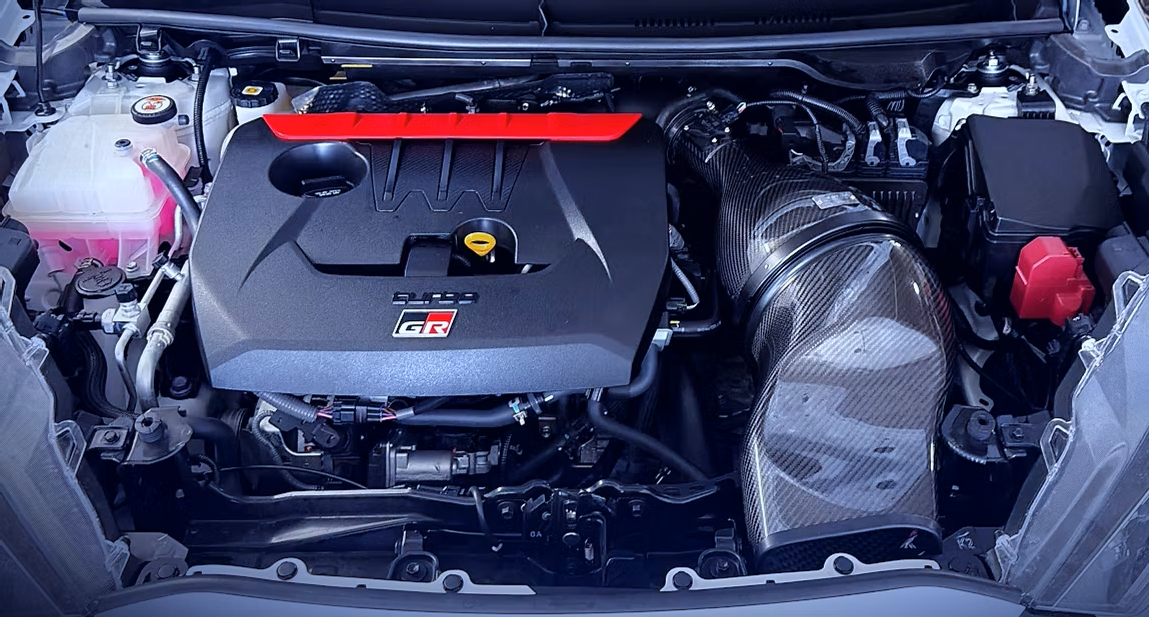 Front view of a car engine bay with a black engine cover labeled 'SUBARU BOXER' and 'GR' with an intake pipe on the right side.
