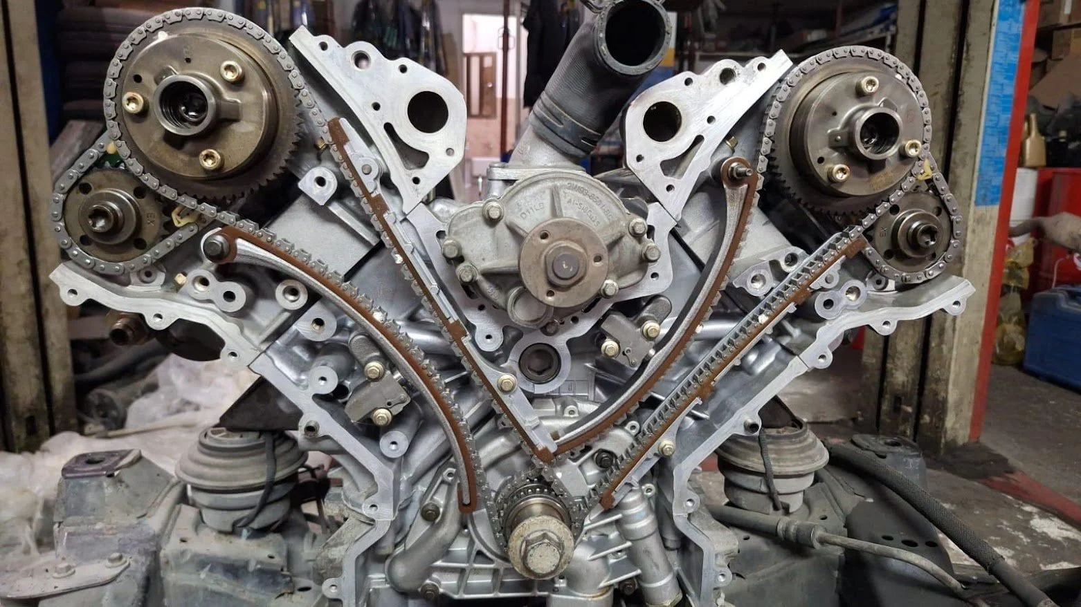 A close-up view of a car engine with timing chains, gears, and pulleys in a workshop setting.