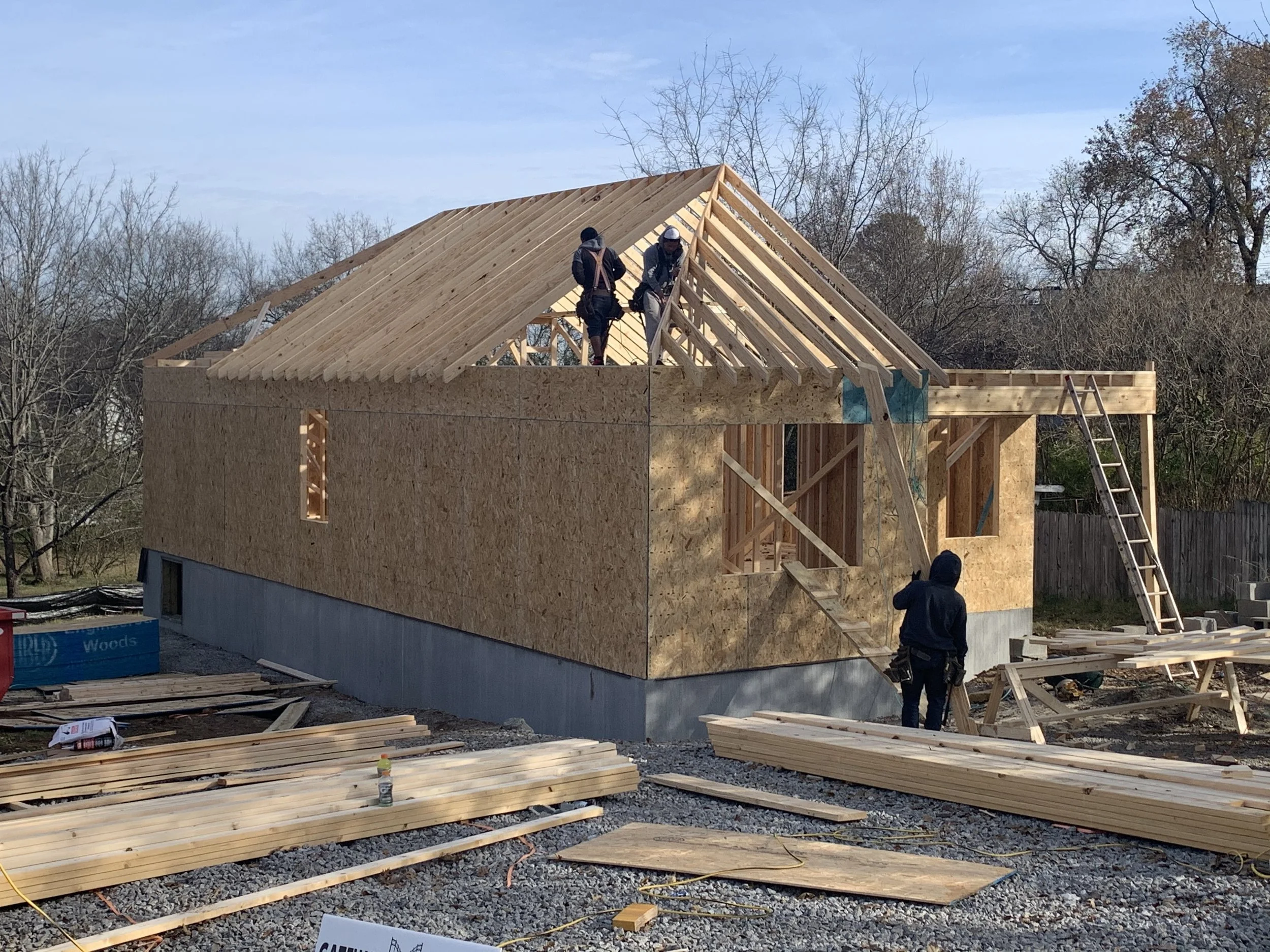 Build to Rent Construction workers building the wooden frame of a house, with the roof partially constructed and plywood walls in place, surrounded by construction materials and tools.