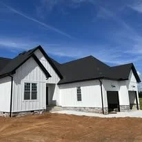 New white house with black roof under a blue sky, surrounded by bare ground.