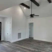 Empty room with white walls, wood flooring, ceiling fan, and ceiling beams.