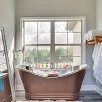 A vintage-style bathroom with an old-fashioned bathtub filled with water and bubbles, positioned in front of a large window with a view outside.
