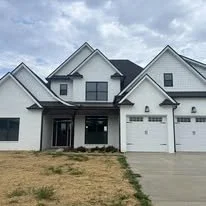 Front view of a modern two-story house with white exterior and attached garage, with a dirt yard in the front.