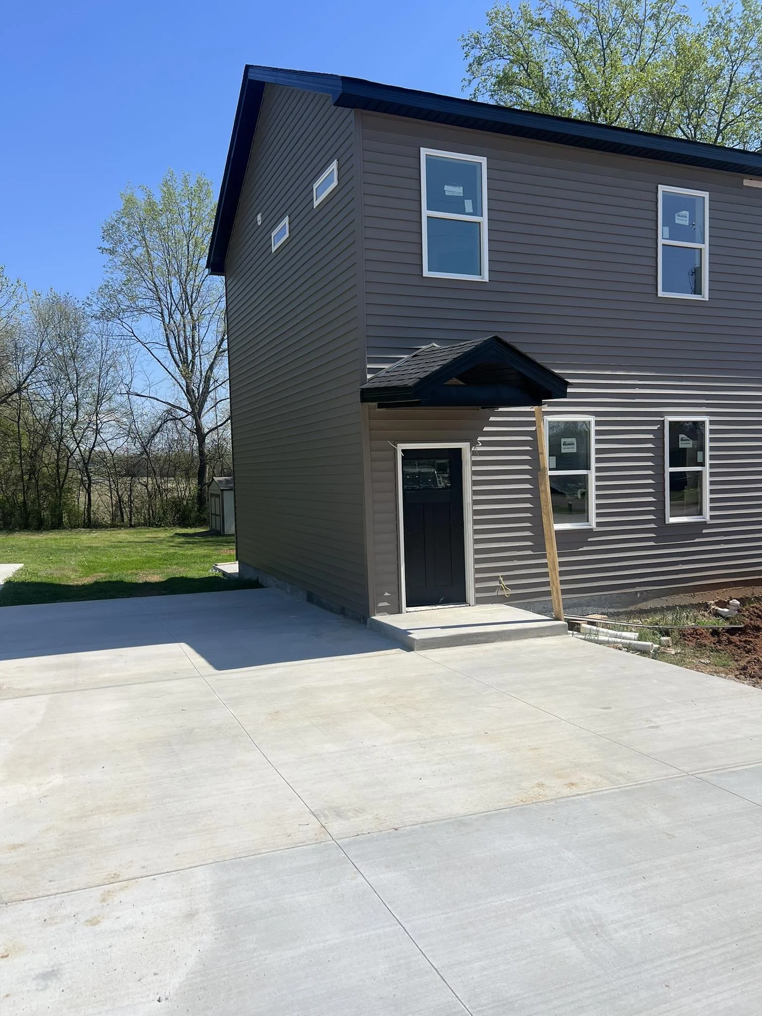 Newly constructed gray house with black roof, multiple windows, small front porch, and fresh concrete driveway. Multi-family Rental