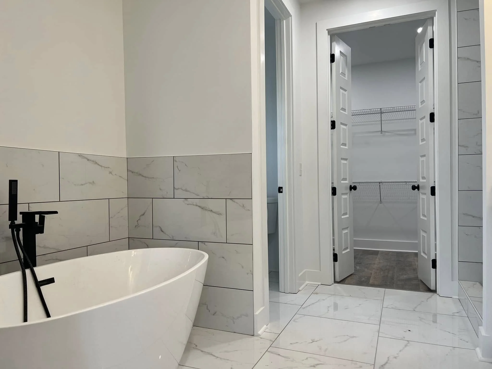 Modern bathroom with a white freestanding bathtub and a walk-in closet with double doors and wire shelving.