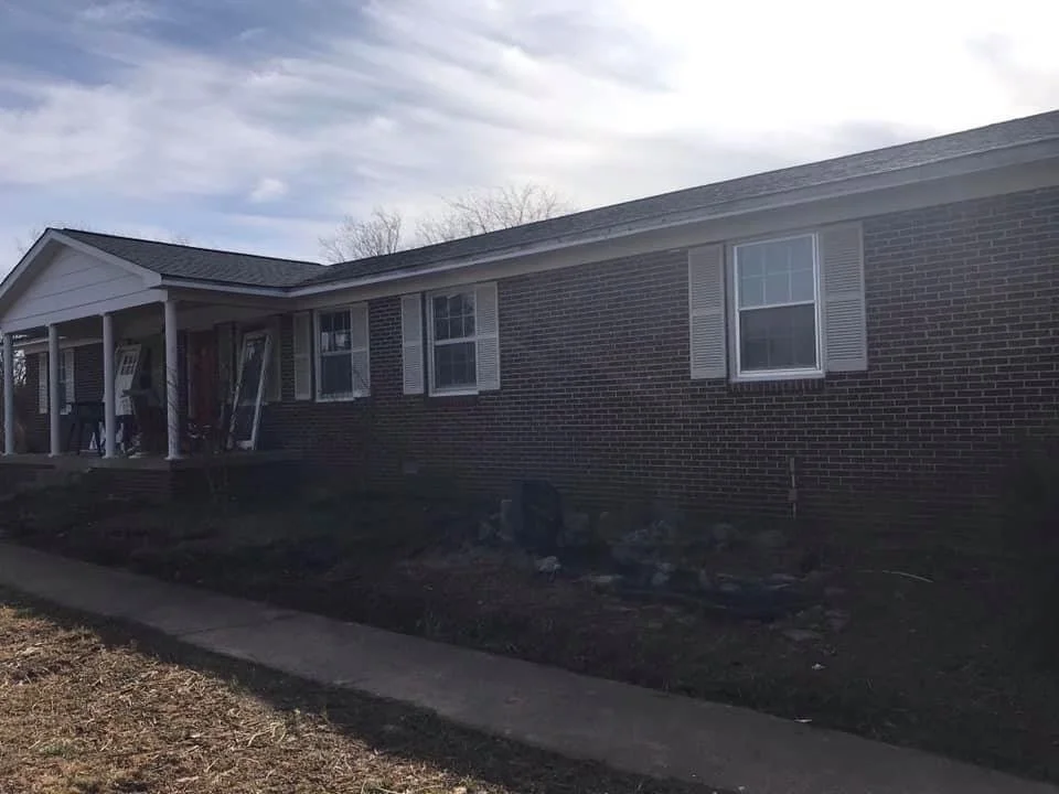A single-story brick house with white window shutters and a front porch under an overcast sky.
