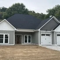 New gray house with white trim, front porch, attached garage, and a dirt yard.